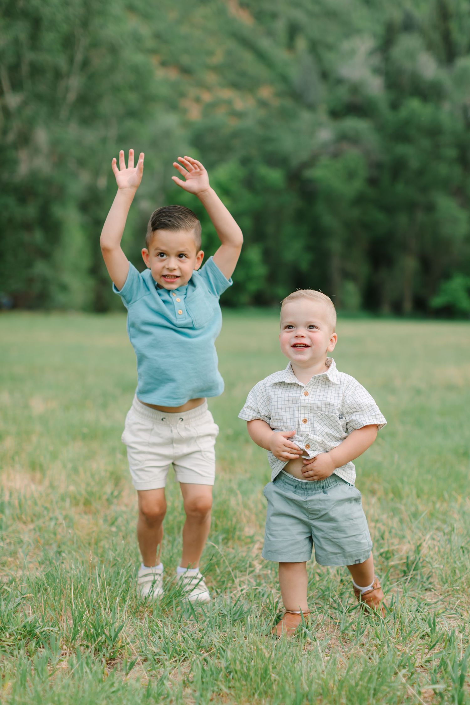 Two young children playing and laughing together in a grassy field on a sunny day.