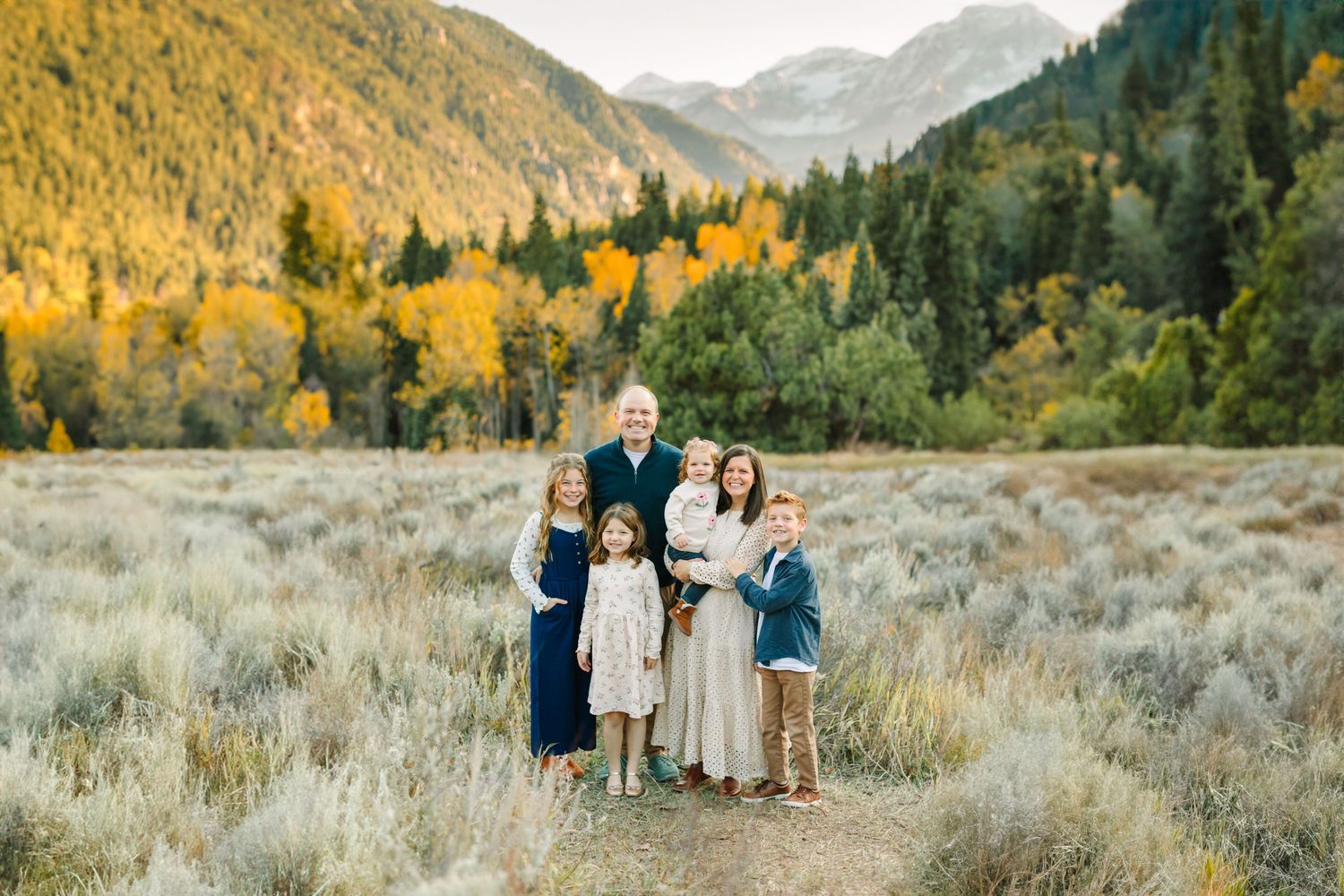 A family stands close together at Tibble Fork Reservoir for their family mini photography session. Fall colors surround them.