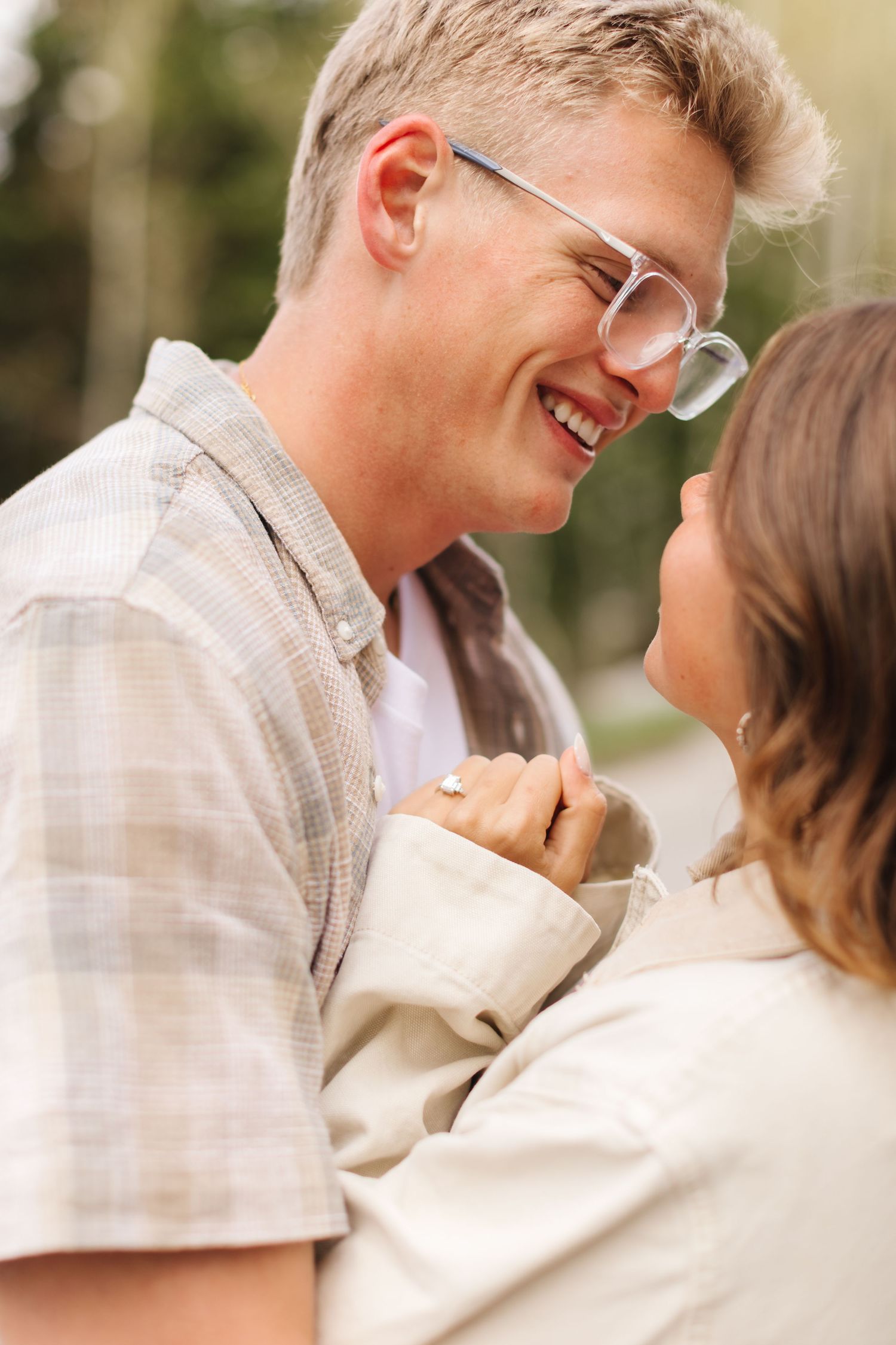 Happy couple sharing a joyful moment outdoors, man with glasses smiling at woman in soft natural light.