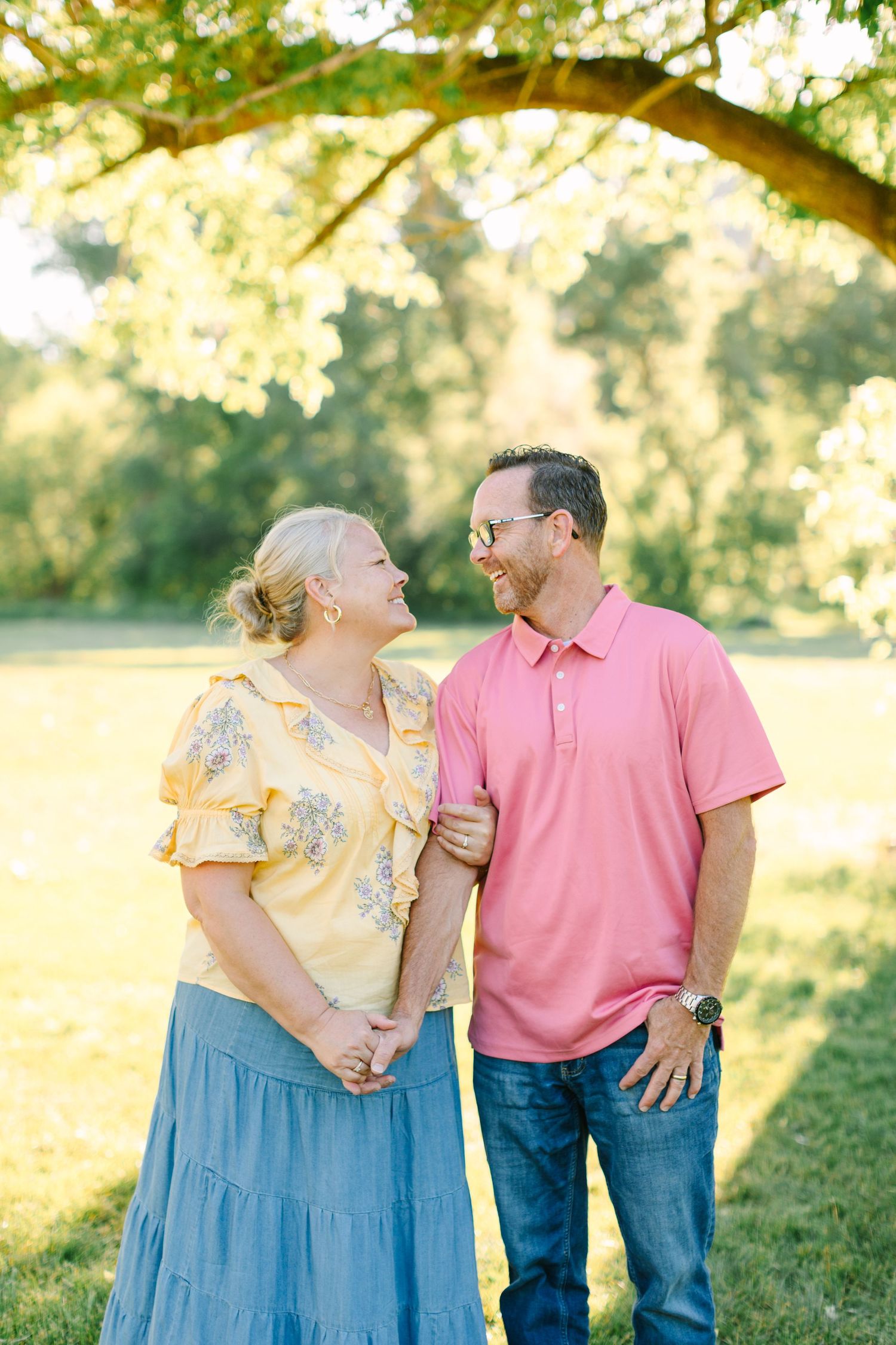 A romantic couple poses together outdoors in a sunlit field wearing coordinating pink and blue outfits.