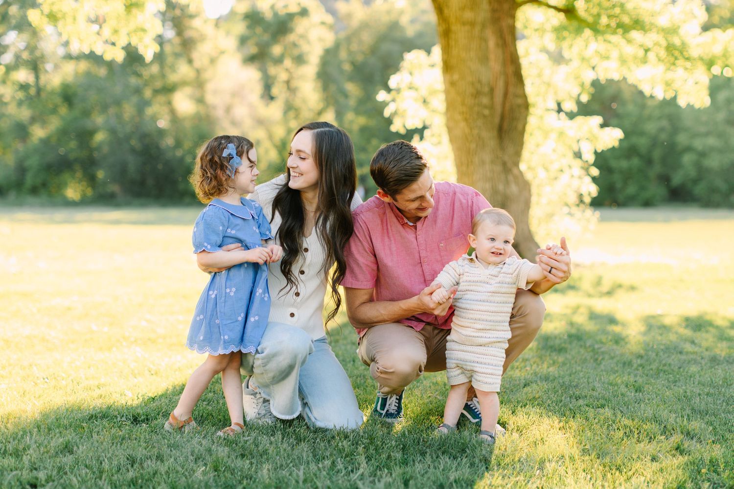 A family sits together on grass in a sunlit park during golden hour, enjoying a warm summer evening.