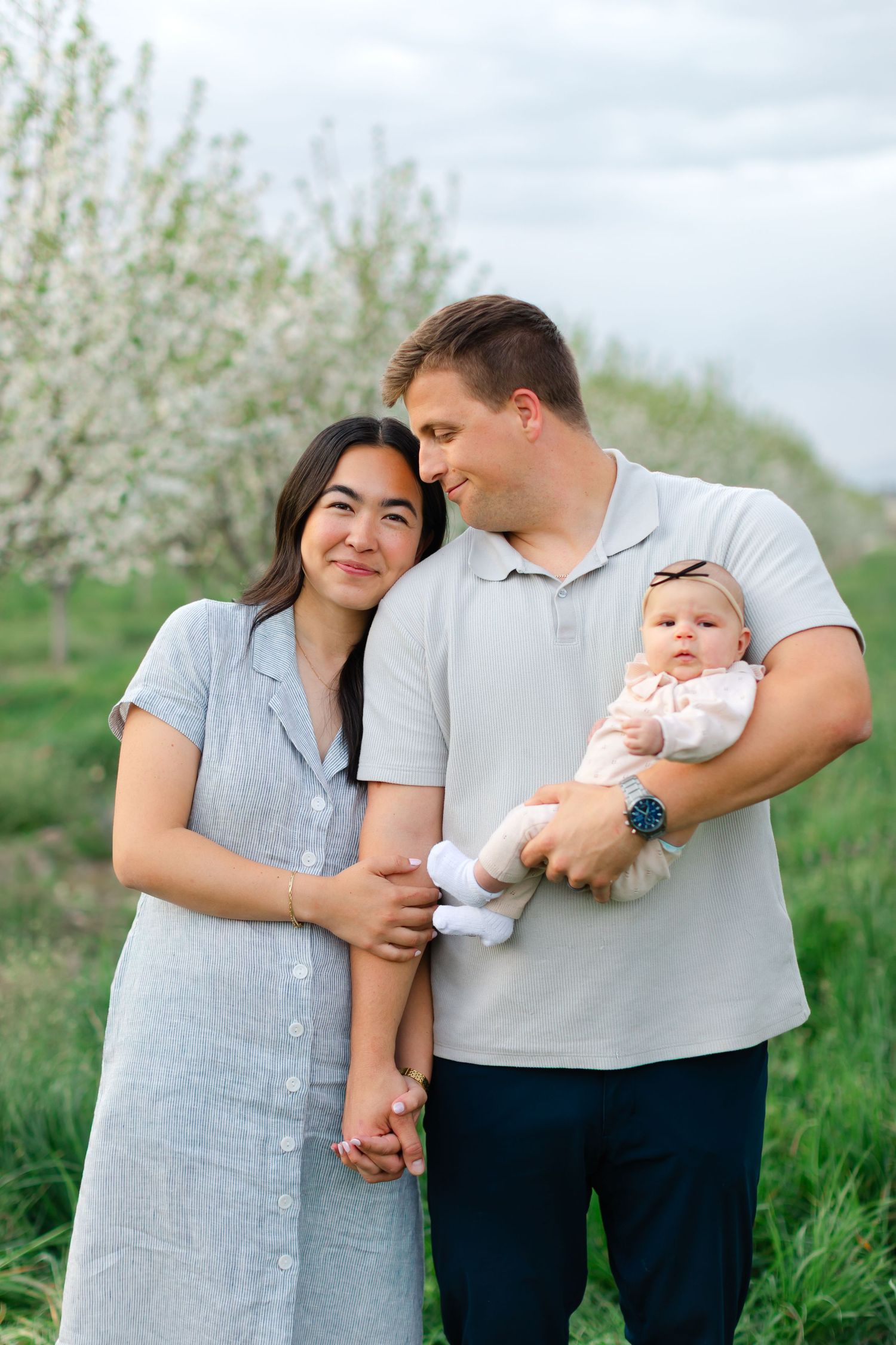 A family stands together in a blooming spring orchard with white blossoms and green grass in the background.