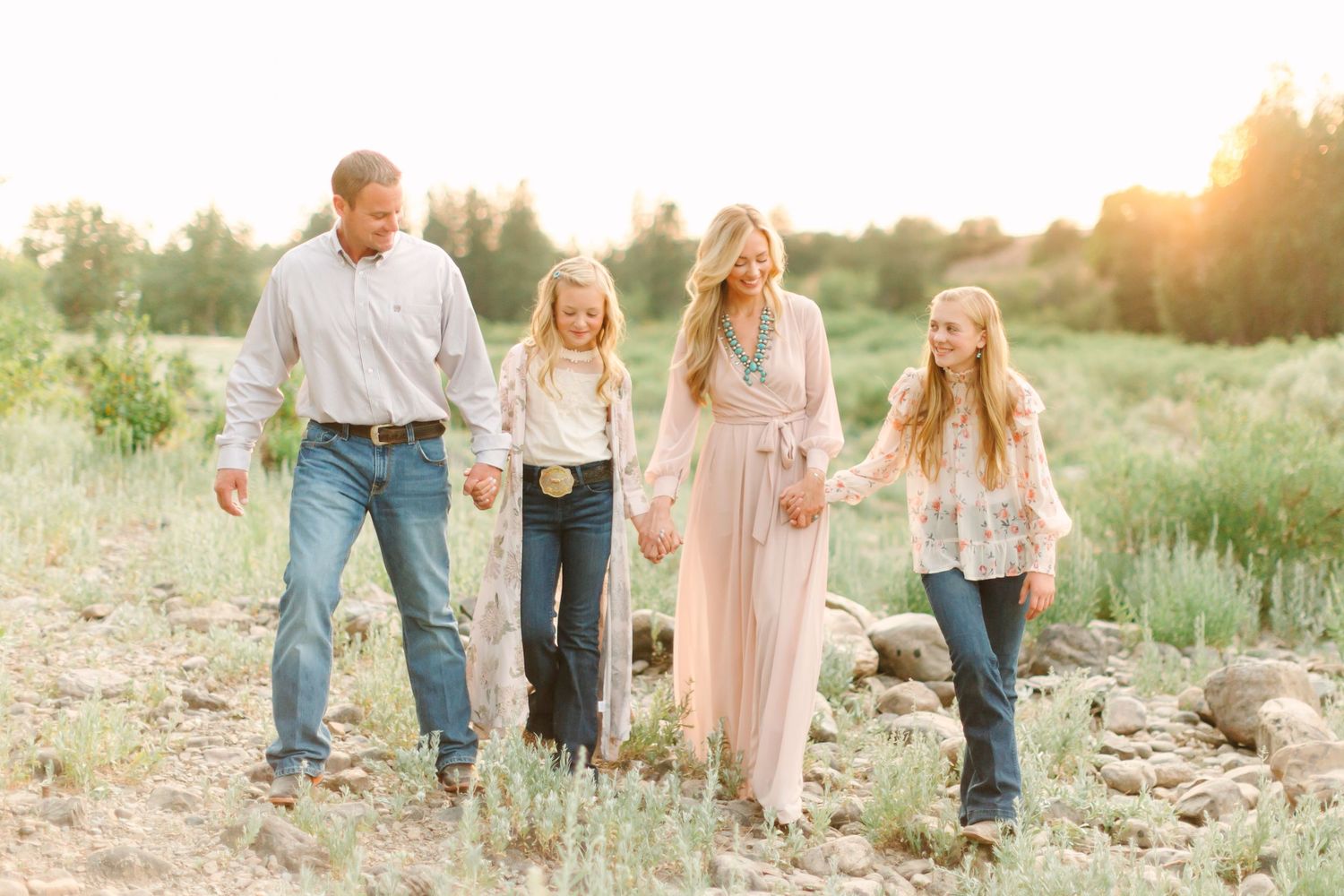 A family walks together through a sunlit meadow wearing coordinated pastel outfits during golden hour.