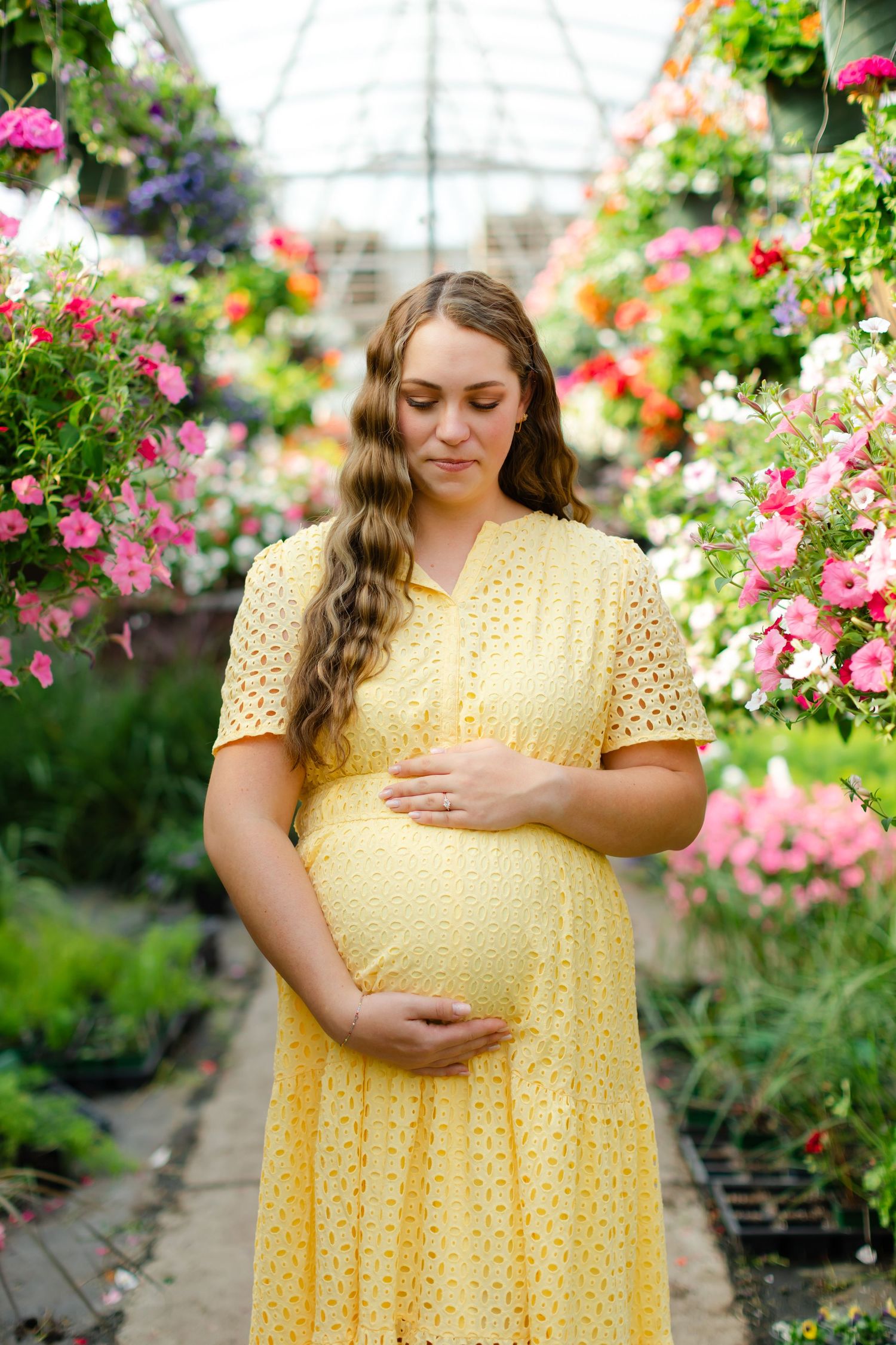 A person in a sunny yellow dress stands among vibrant pink flowers in a greenhouse nursery.