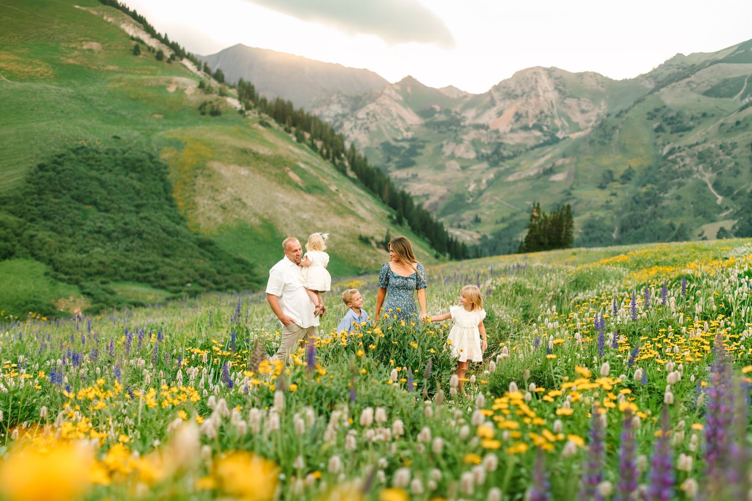 Family walking through a vibrant wildflower meadow with mountain backdrop at sunset.