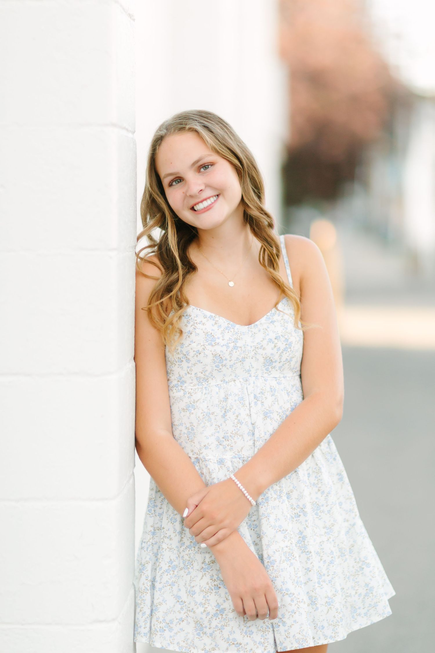Three photos of a young girl in a white floral dress posing outdoors against a light colored wall.