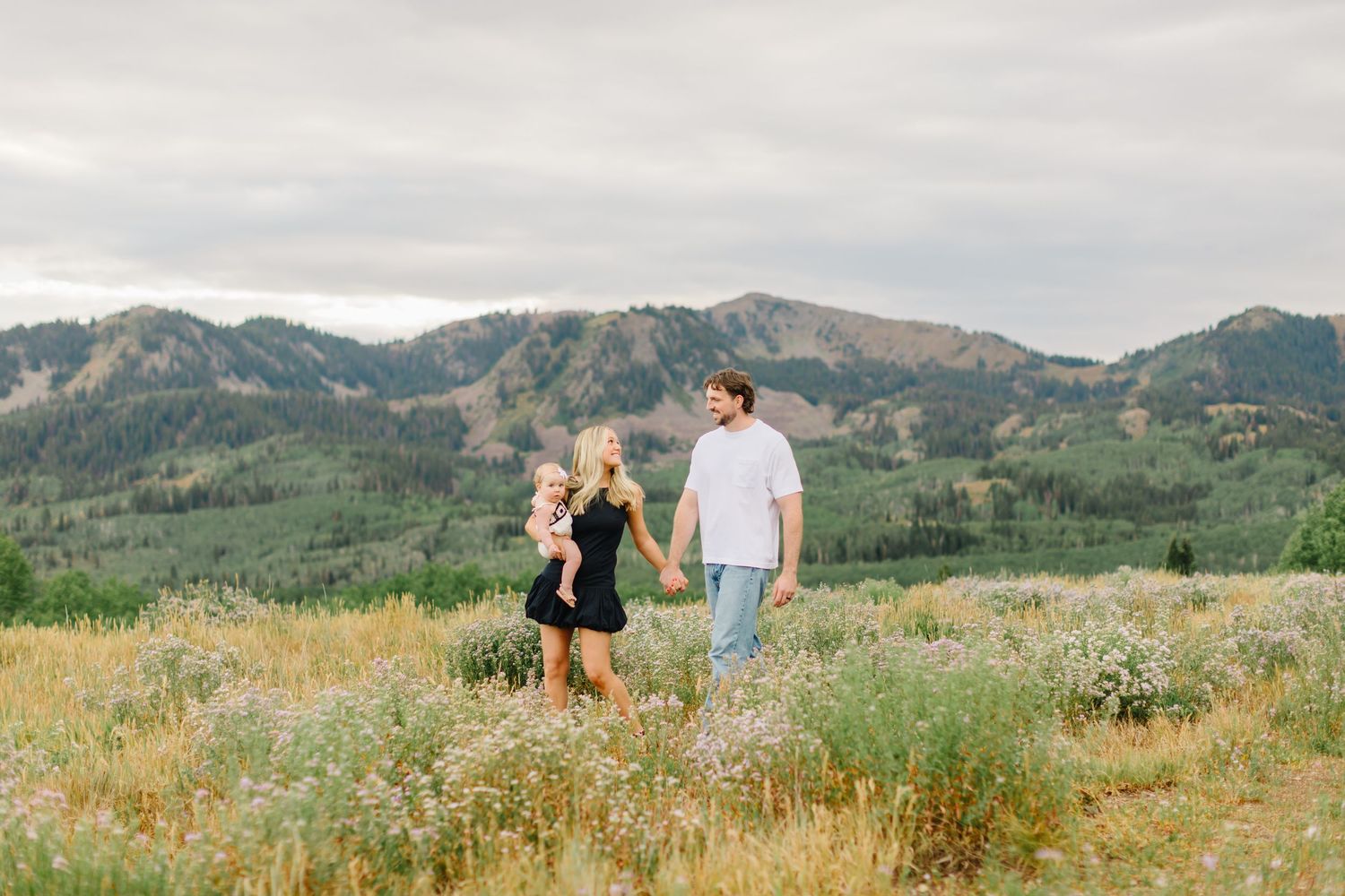 A couple walks through a scenic mountain meadow filled with wildflowers on a summer afternoon.