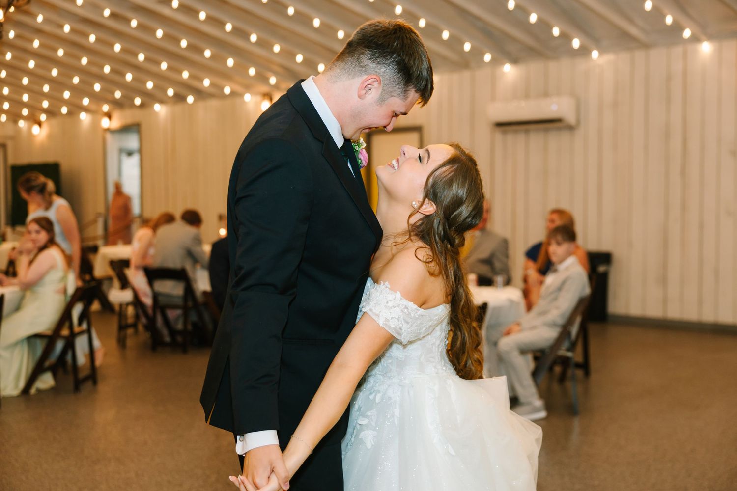 A romantic first dance between newlyweds at a wedding reception under twinkling string lights.