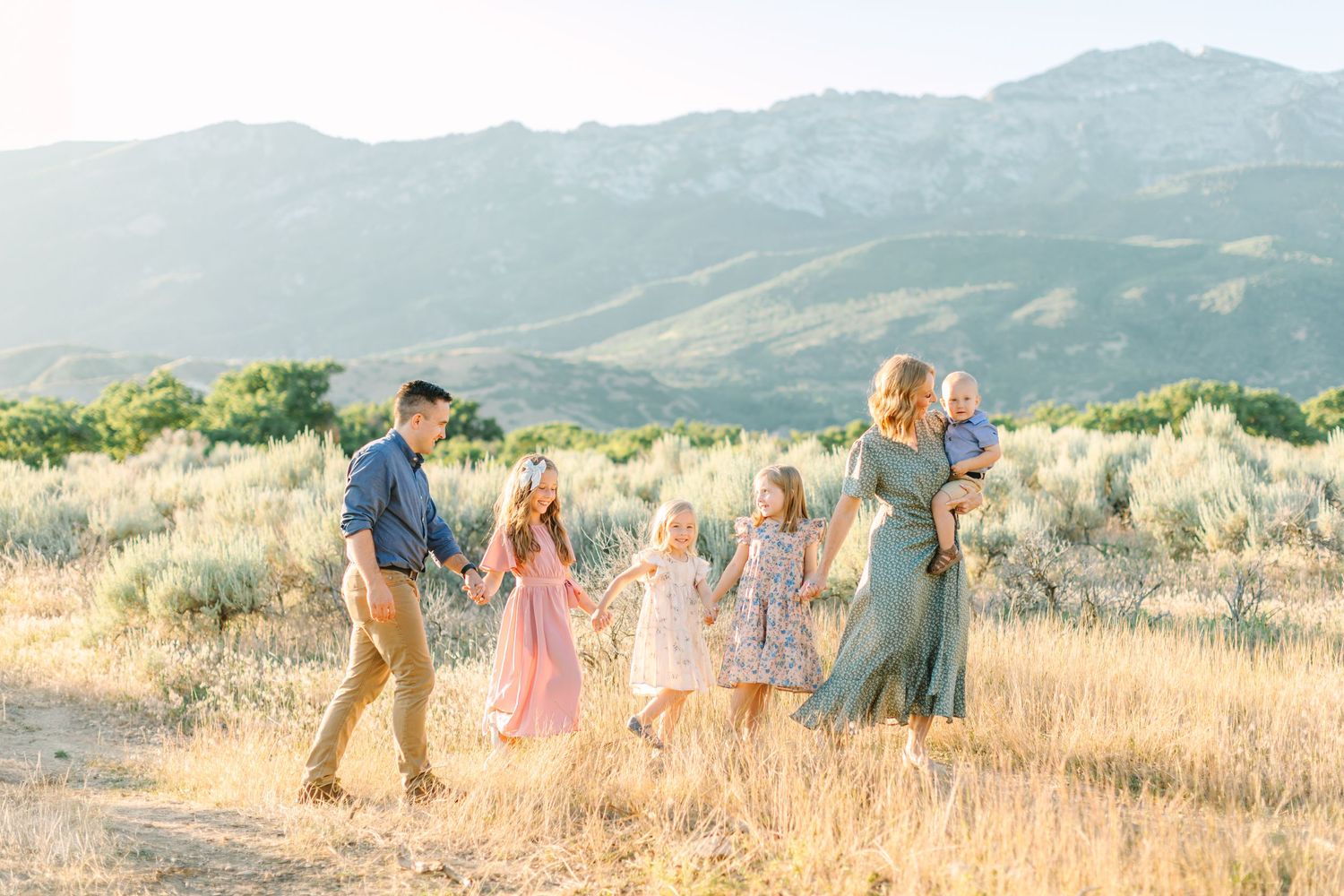 A group walks together through golden grass fields with mountains in the background during sunset.