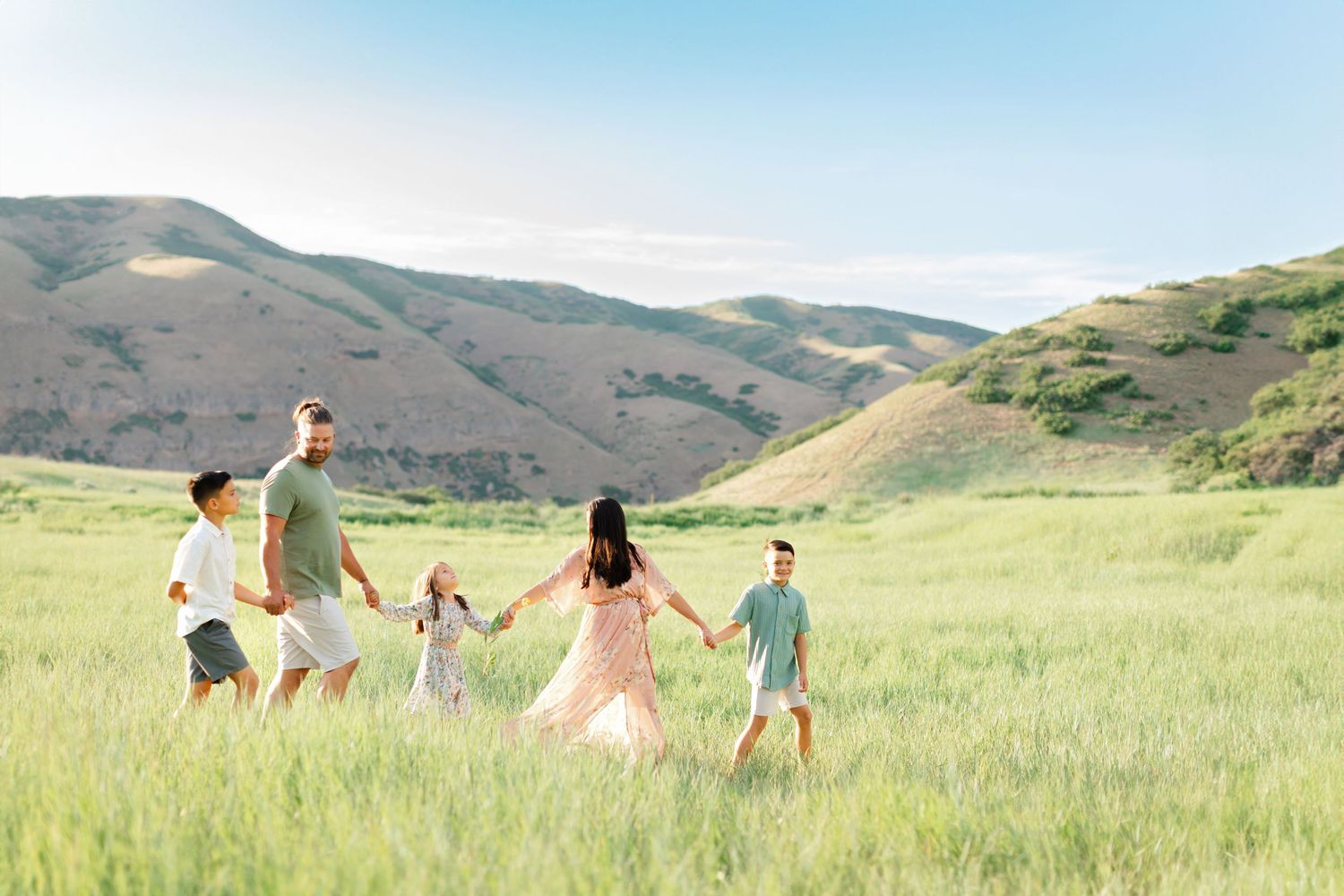 A group of people walk together through a scenic green hillside meadow on a sunny summer day.