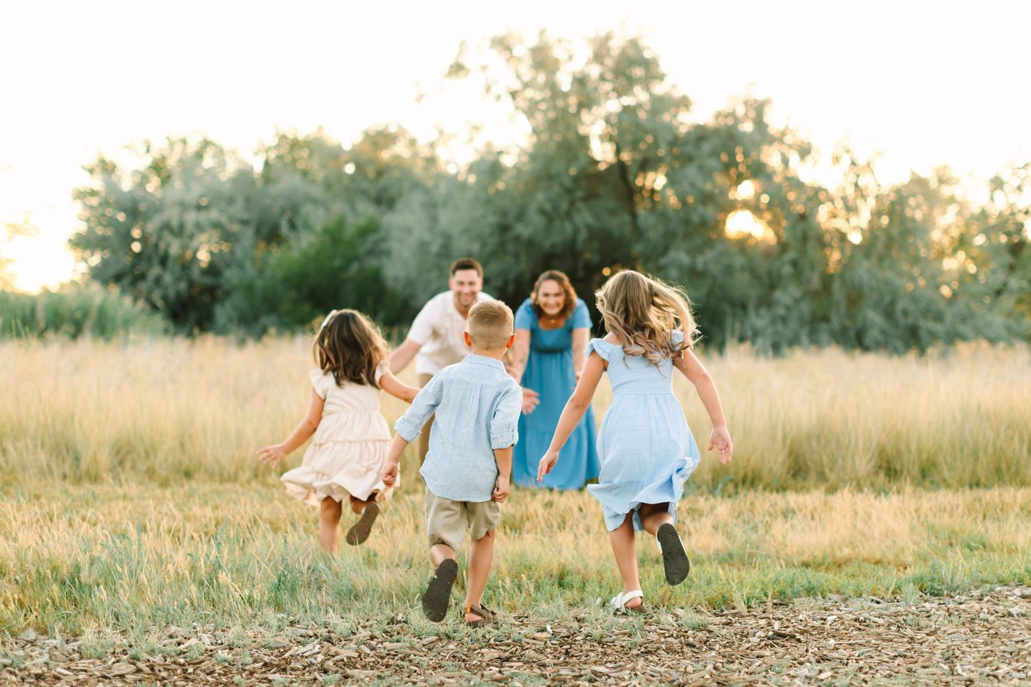 Family running together in a golden sunlit field with lush green trees in the background during sunset in Bountiful, Utah.