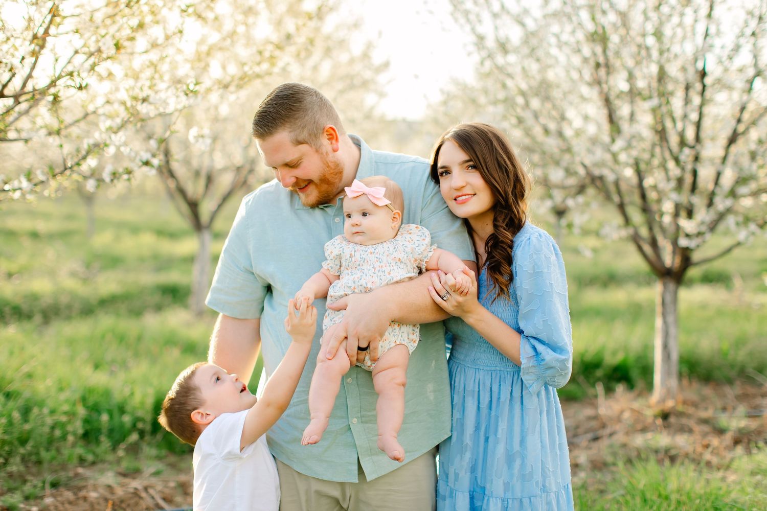 A young family amongst beautiful orchard blossoms for their family photoshoot in Santaquin, Utah.