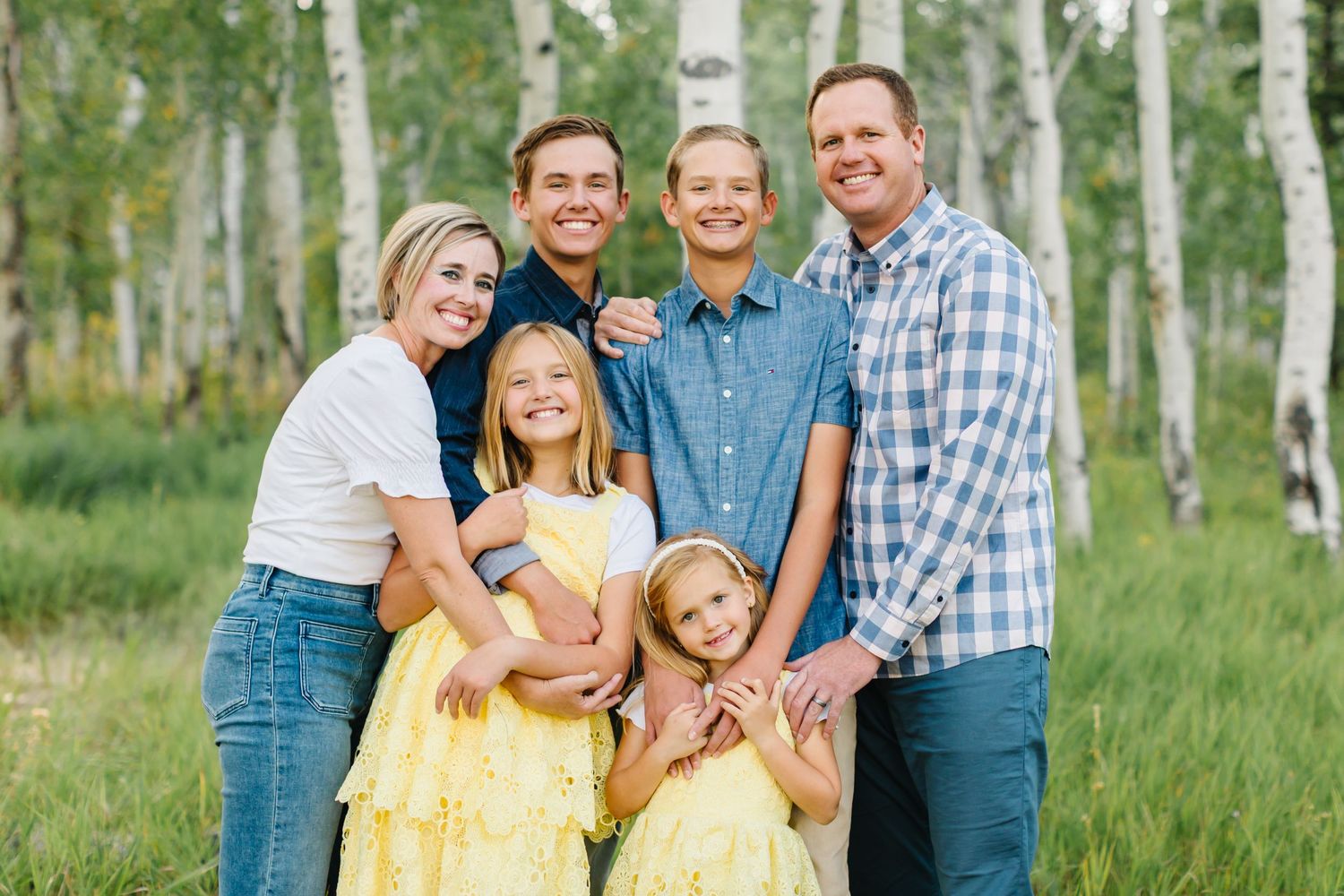 A happy family poses together in a scenic aspen grove wearing coordinated blue and yellow outfits.
