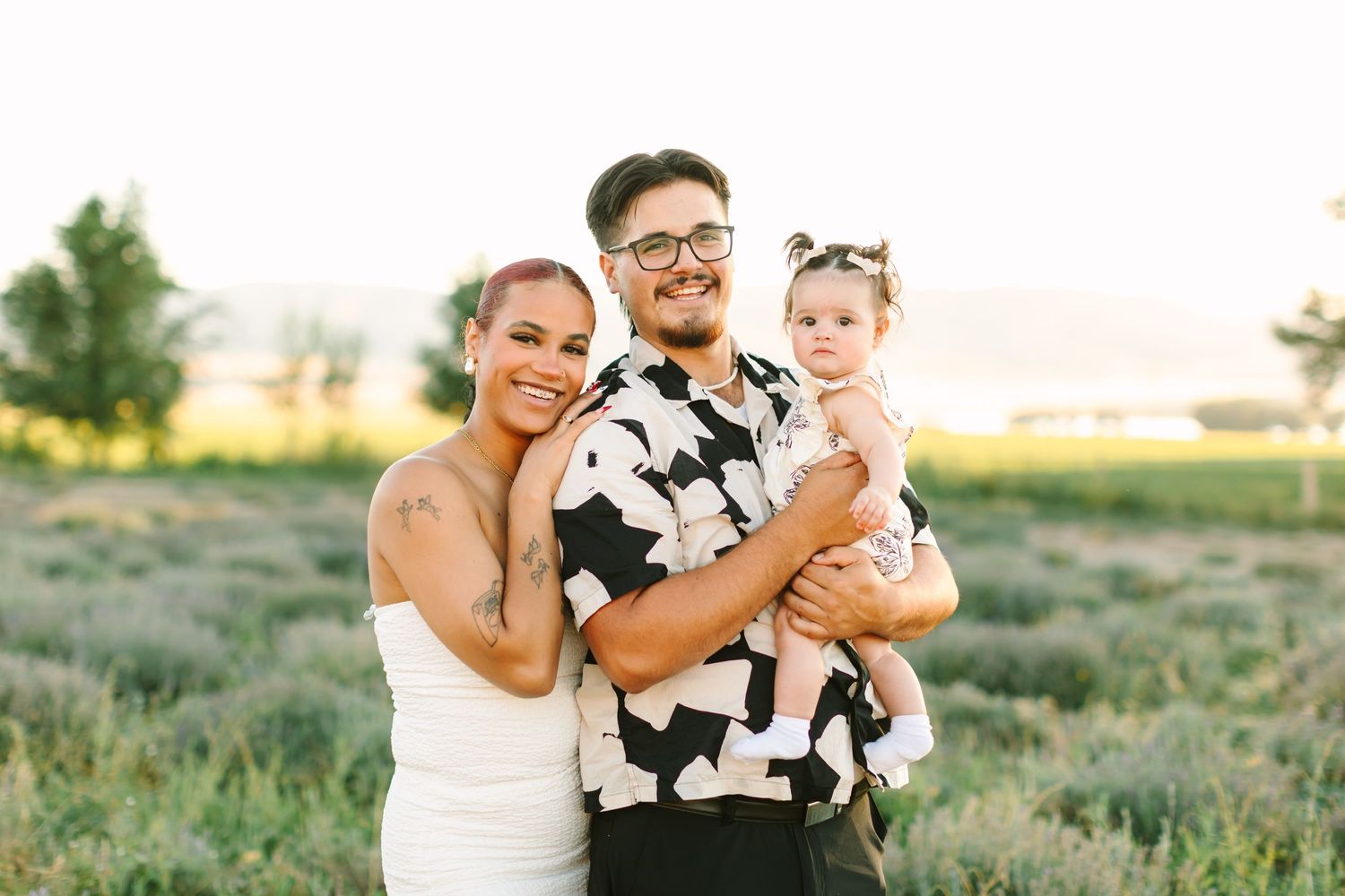 A family poses together in a field at sunset wearing coordinated black and white outfits.