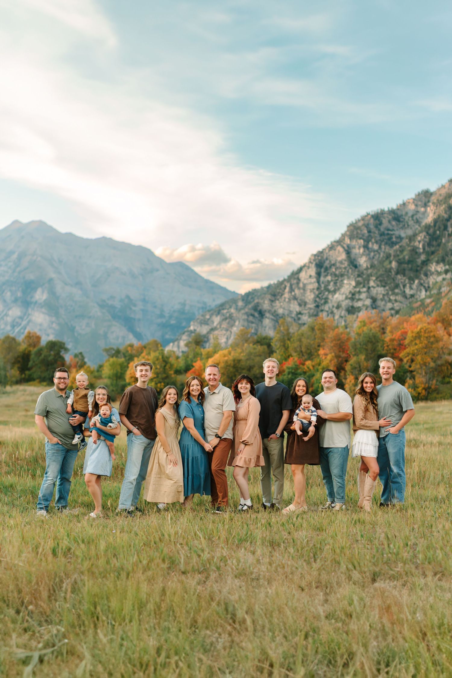 An extended family is standing on tall grass, surrounded by mountains and fall foliage for their family photoshoot at Buffalo Peak in Provo.