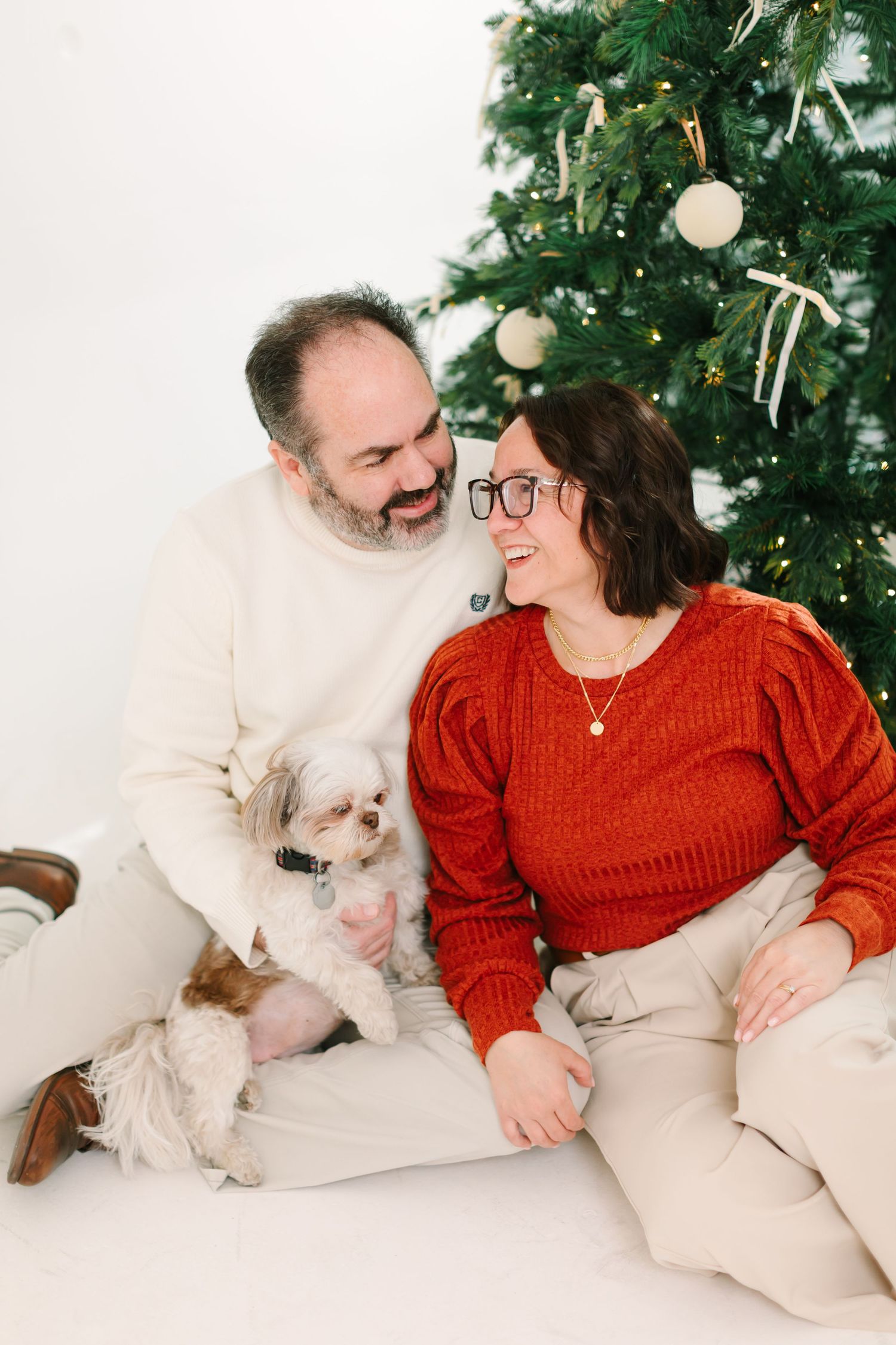 Couple and their small white dog share joyful moment by Christmas tree at White Space Studios in Provo, Utah in Utah County..