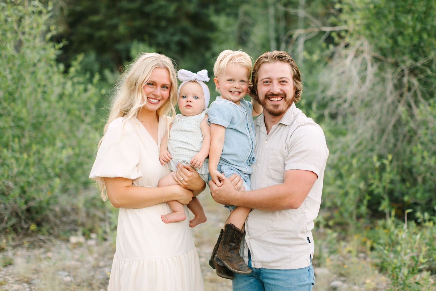 Large family group smiling outdoors in coordinated sage green and white outfits with lush green trees behind in Provo, Utah.