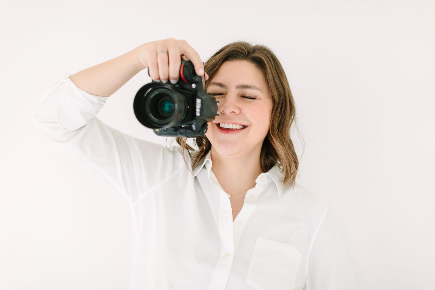 A person smiles while holding a professional camera in a bright white studio setting.