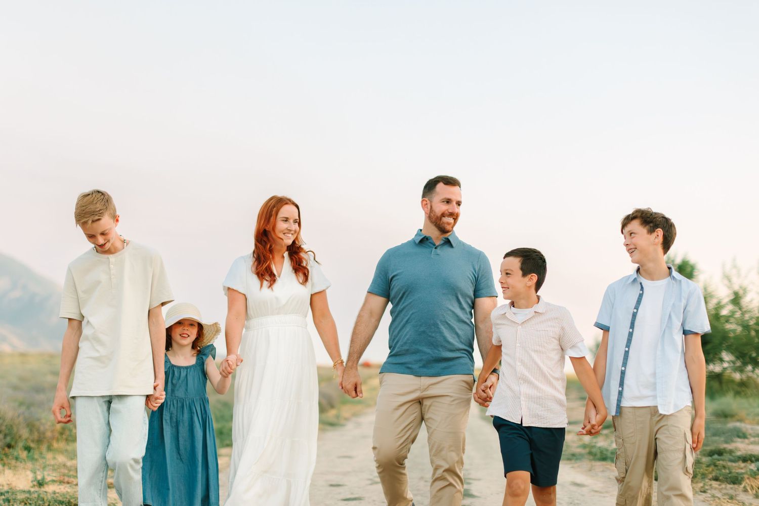 Family wearing coordinated casual outfits in teal and white walking together on a beach during sunset.