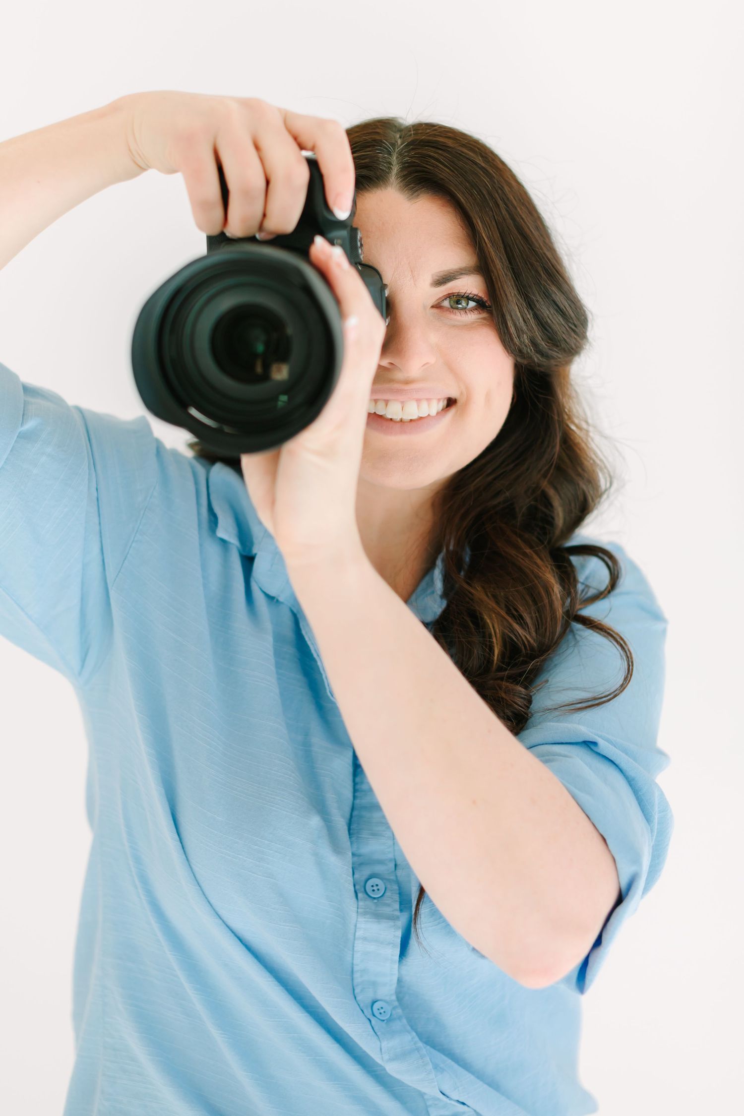 A photographer in a blue shirt takes photos with a professional camera against a white background.