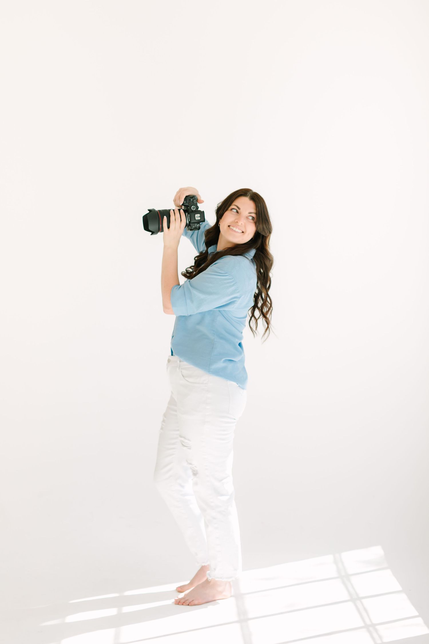 A photographer in light blue shirt and white pants takes pictures from three different angles against a white backdrop.