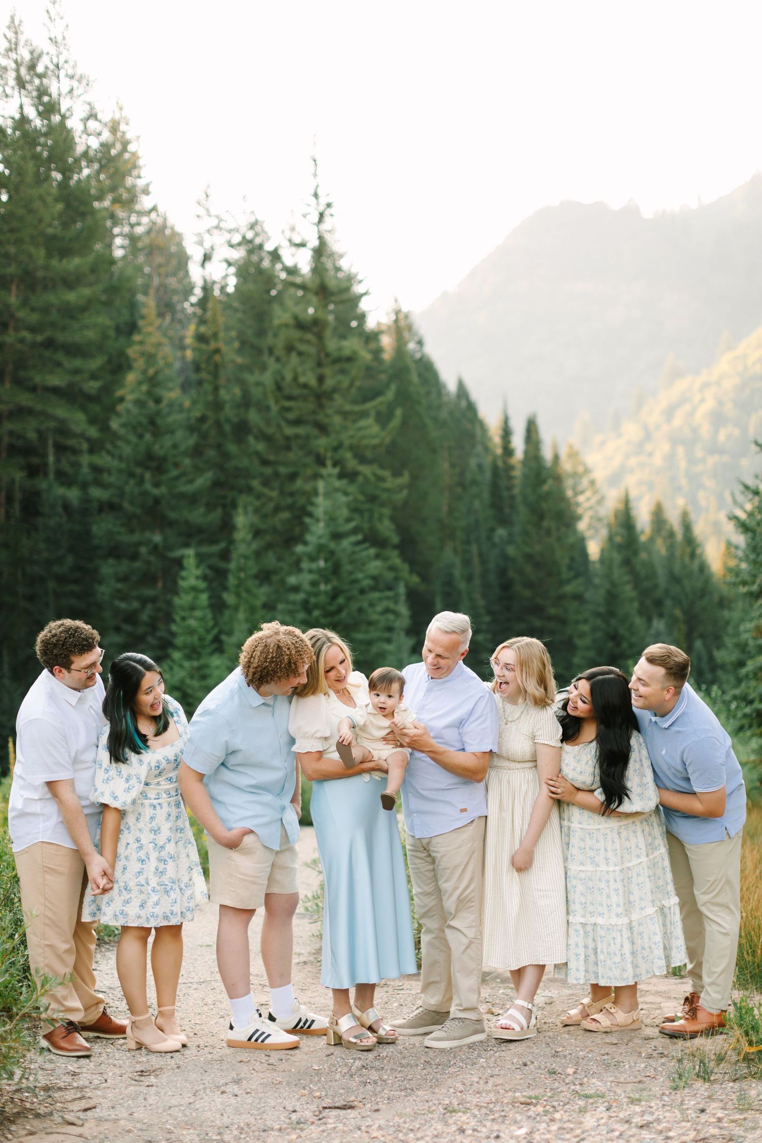 Large family gathering outdoors on a mountain trail surrounded by tall pine trees, sharing a joyful moment together in Utah.