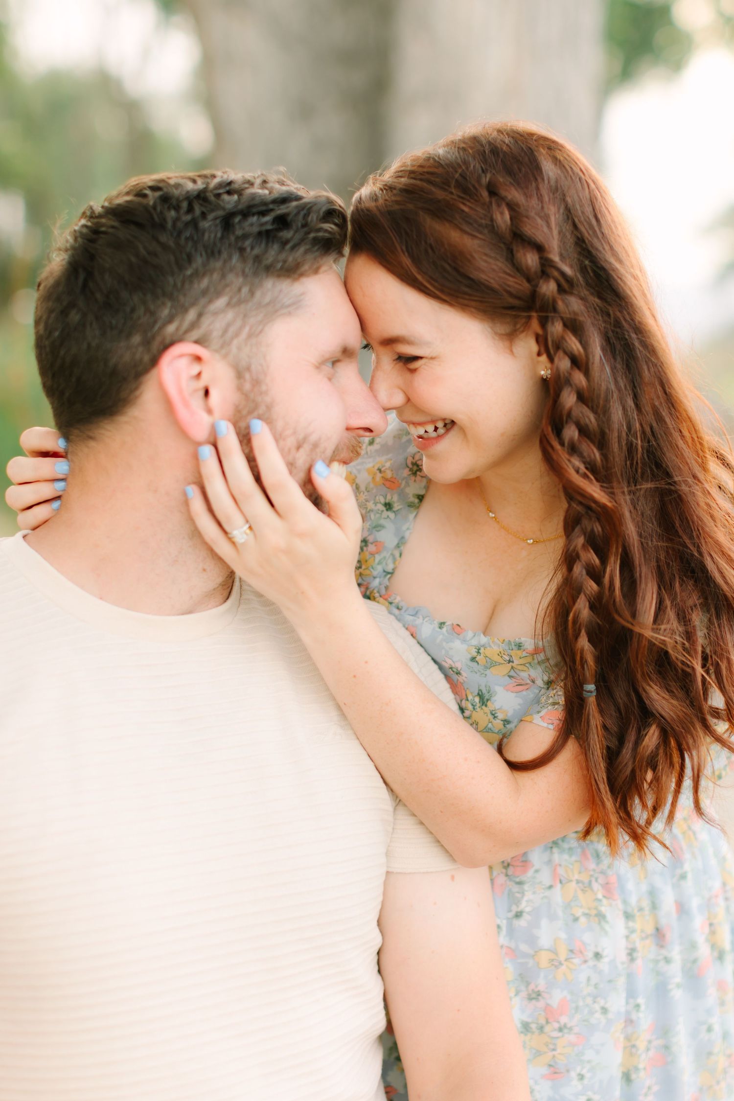 Smiling couple with foreheads touching, woman with red braided hair holding mans face tenderly.