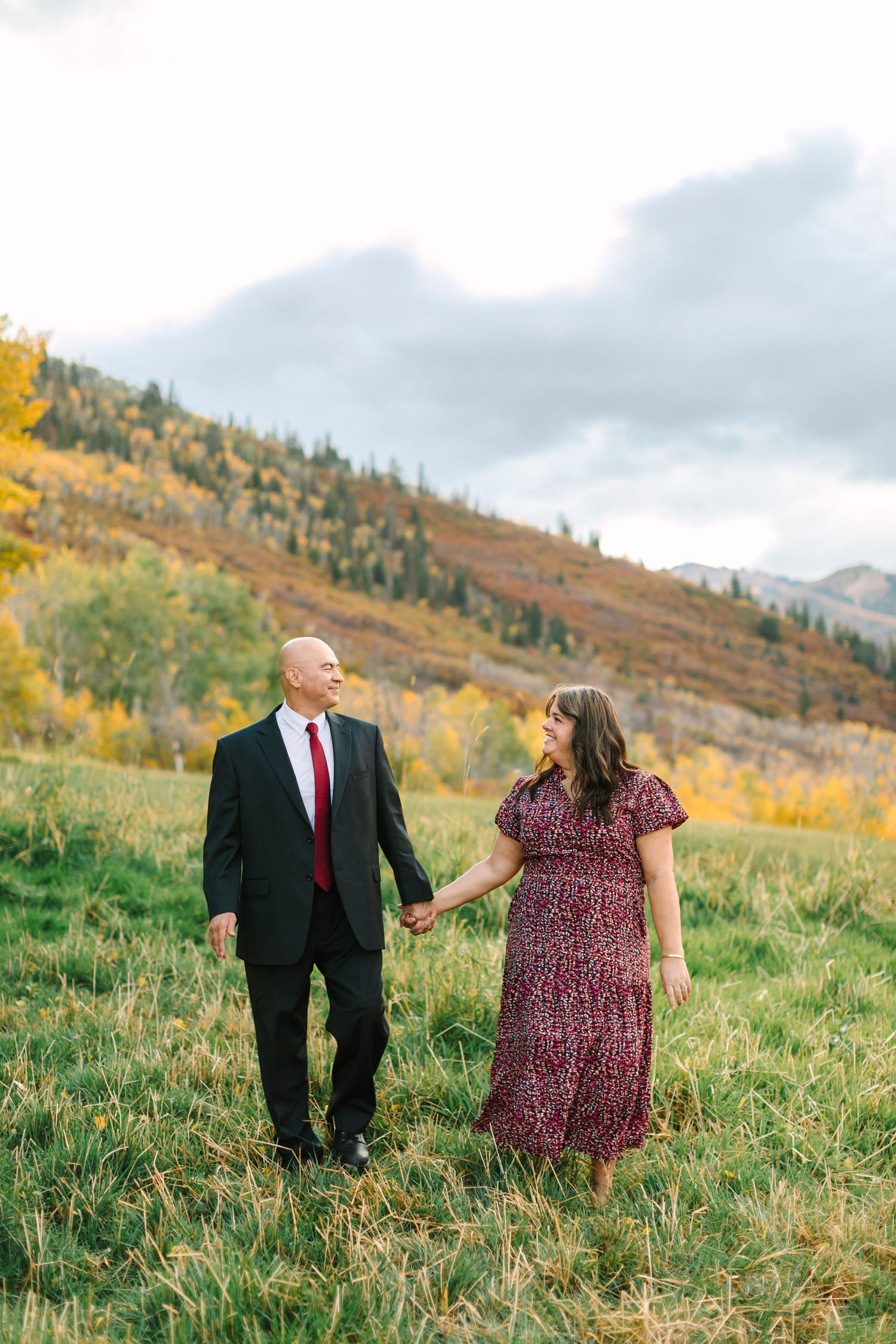 Couple walking together through a scenic autumn mountain meadow with golden foliage in the background.