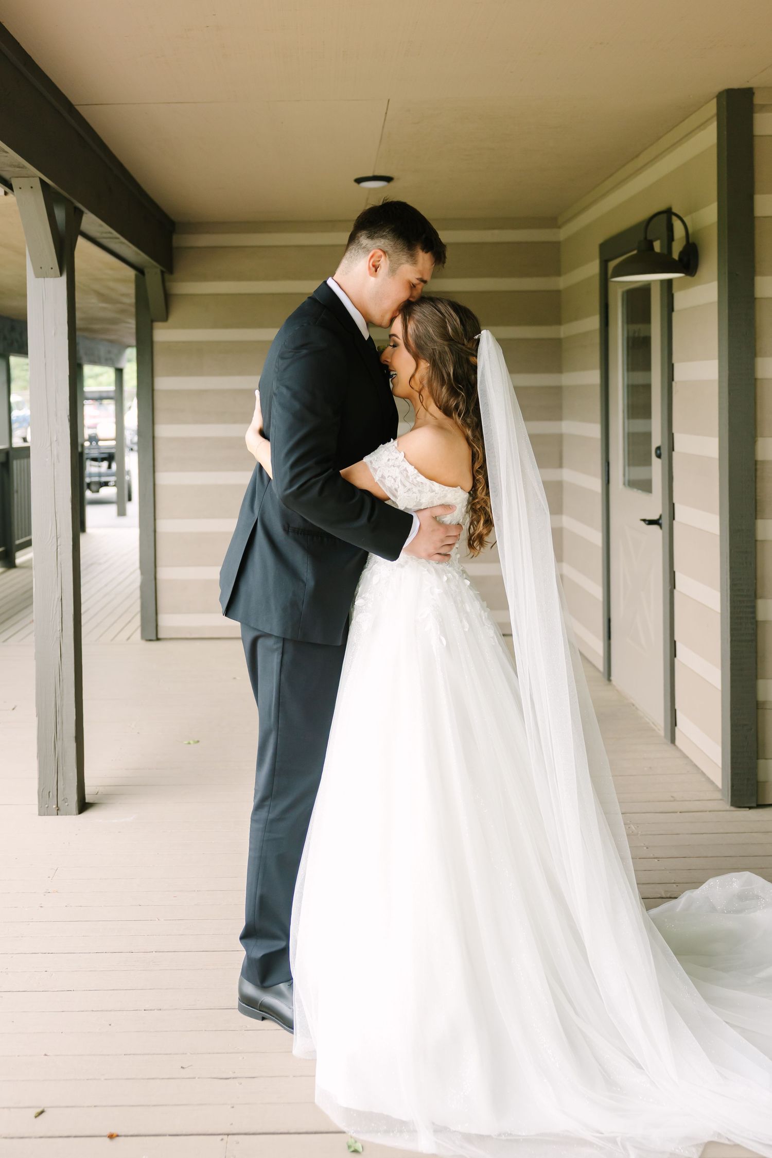 A romantic wedding couple shares intimate kisses in a covered walkway with white columns.