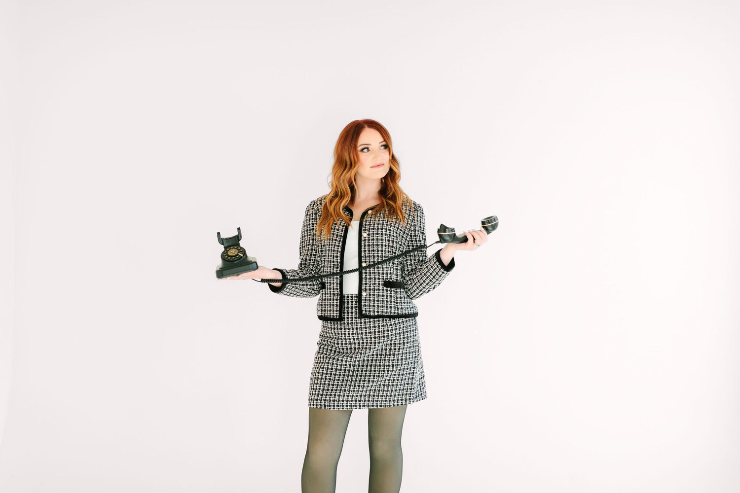 Woman in houndstooth print blazer and matching pants poses with arms outstretched against white background.