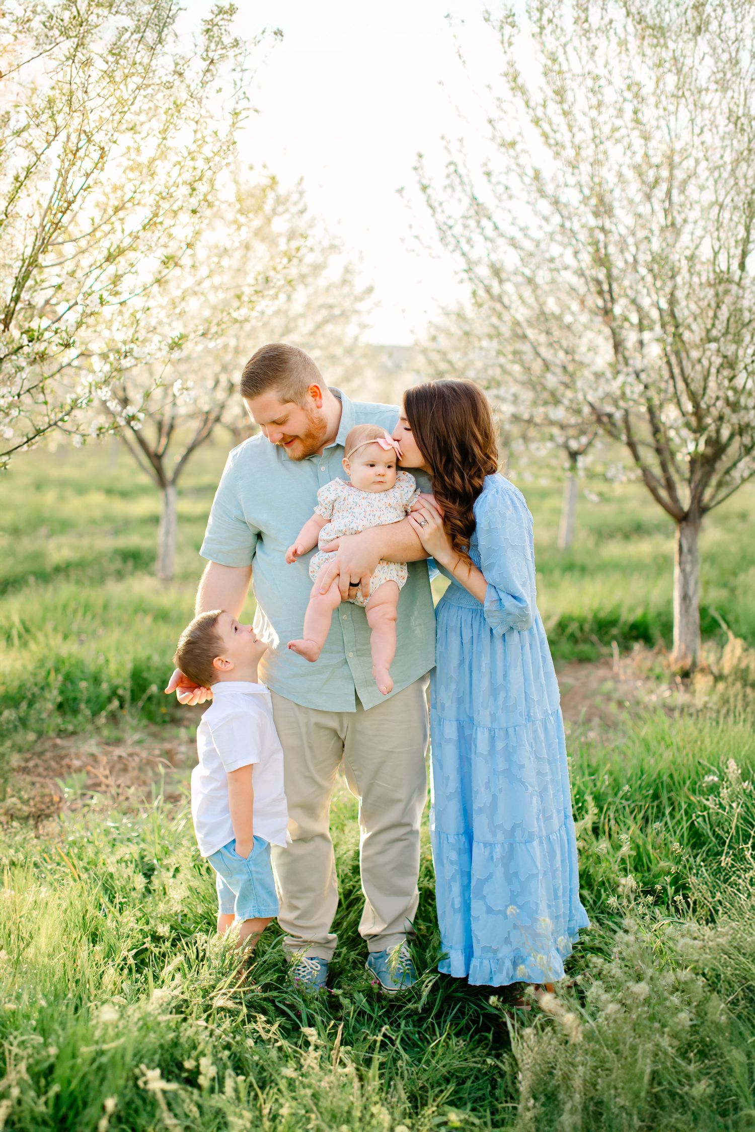A family plays together in green grass at a blooming orchard for their family photoshoot in Santaquin, Utah.