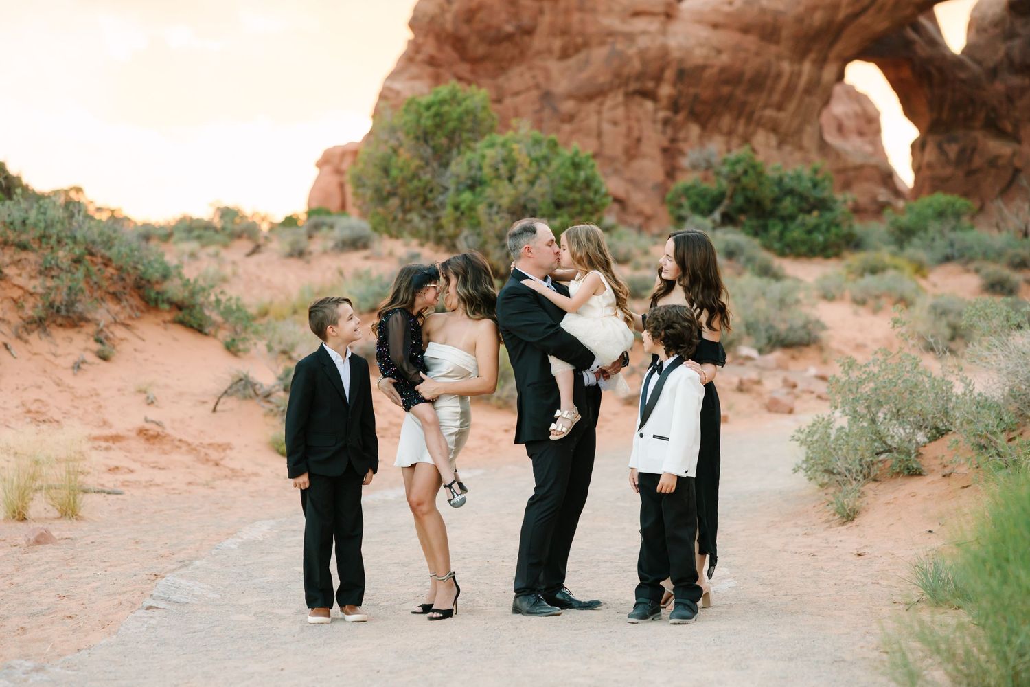 A small group stands together on a desert path with red rock formations and desert vegetation in the background.