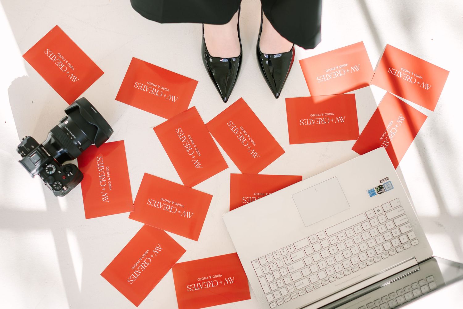 Flatlay of red gift cards scattered on white surface with keyboard and black shoes in frame.