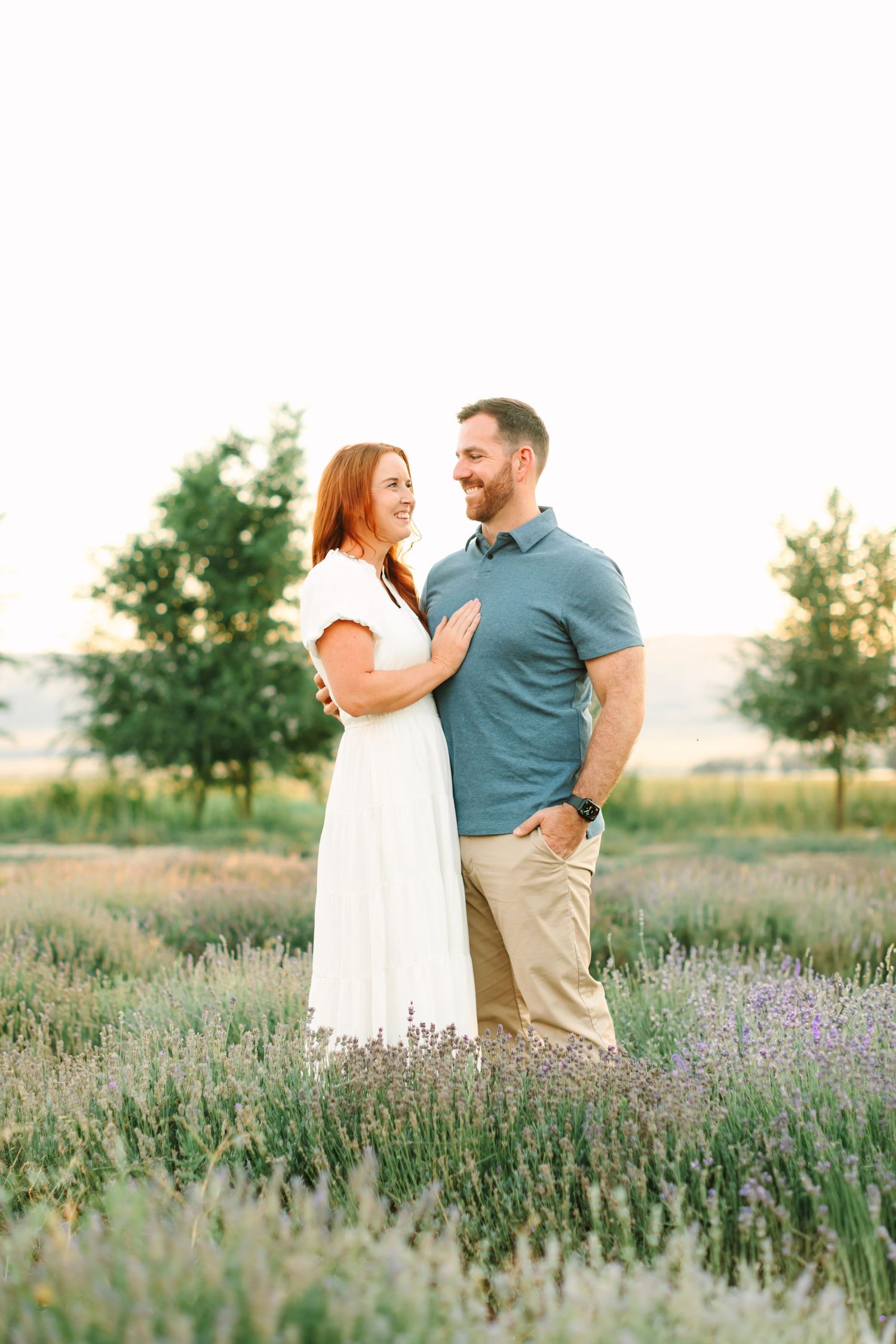 A couple shares a joyful moment together while standing in a blooming lavender field at sunset.