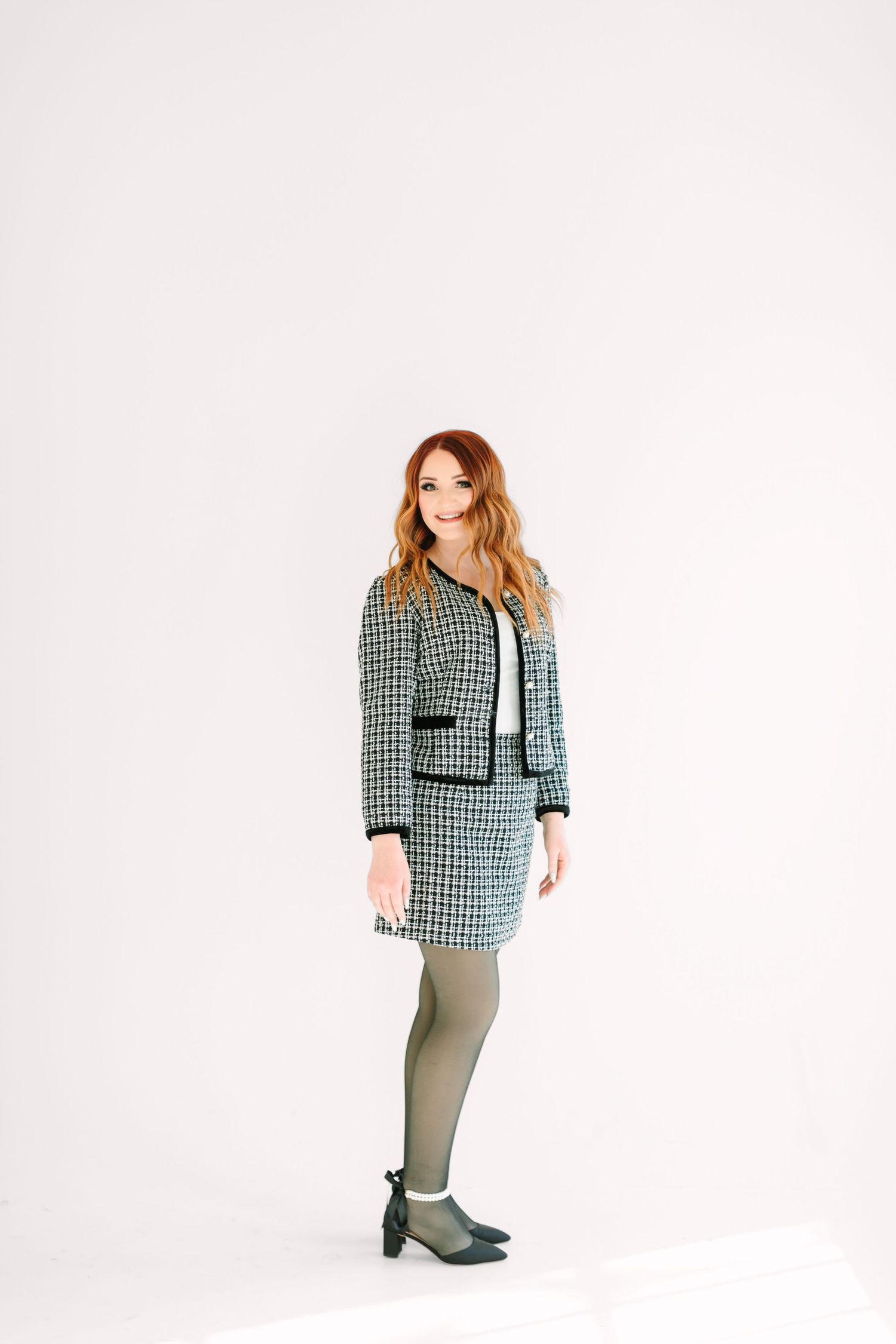 A model poses in a black and white houndstooth jacket with matching skirt against a white studio background.