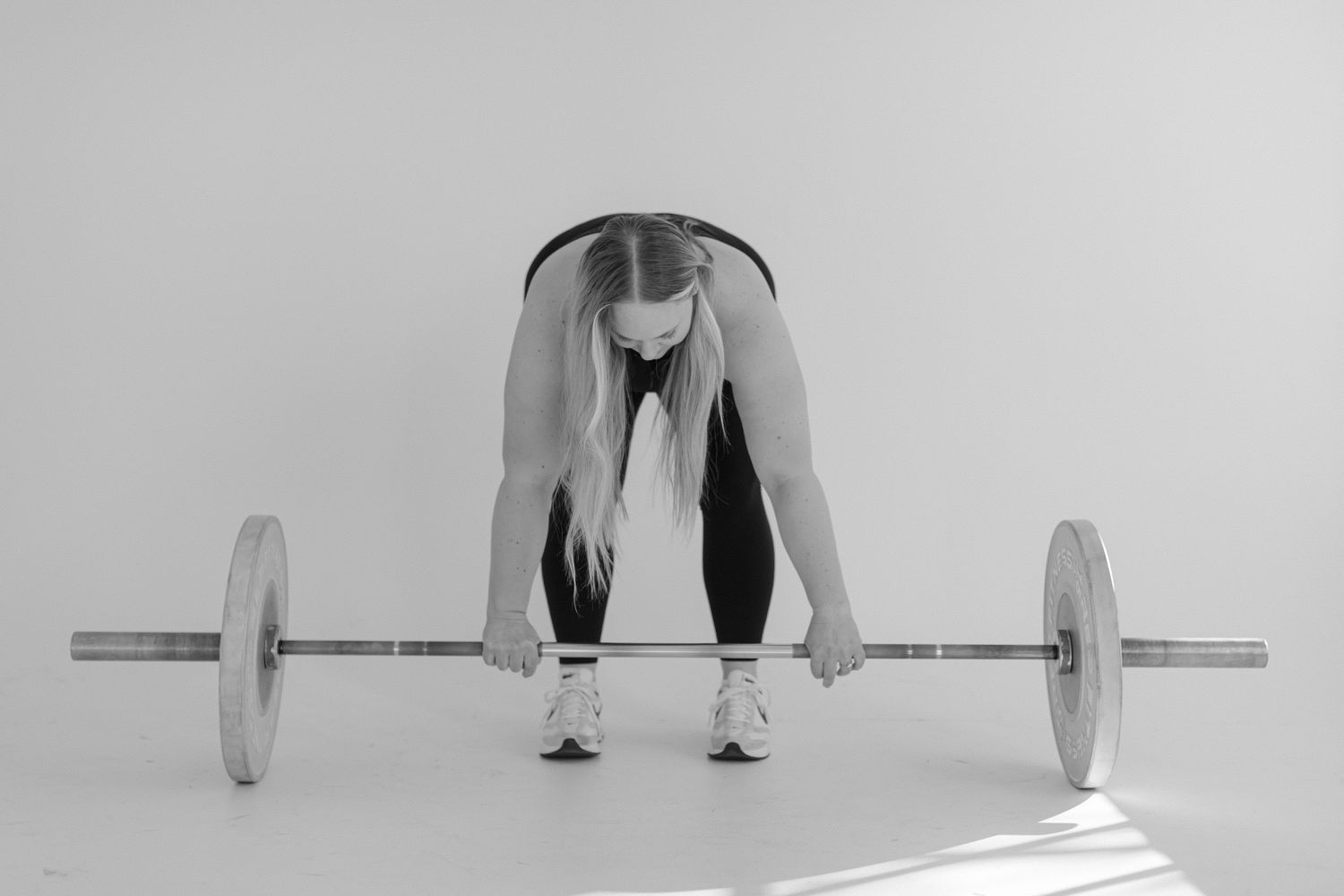 A sequence of exercise poses demonstrating proper form for a barbell deadlift movement from start to finish position.
