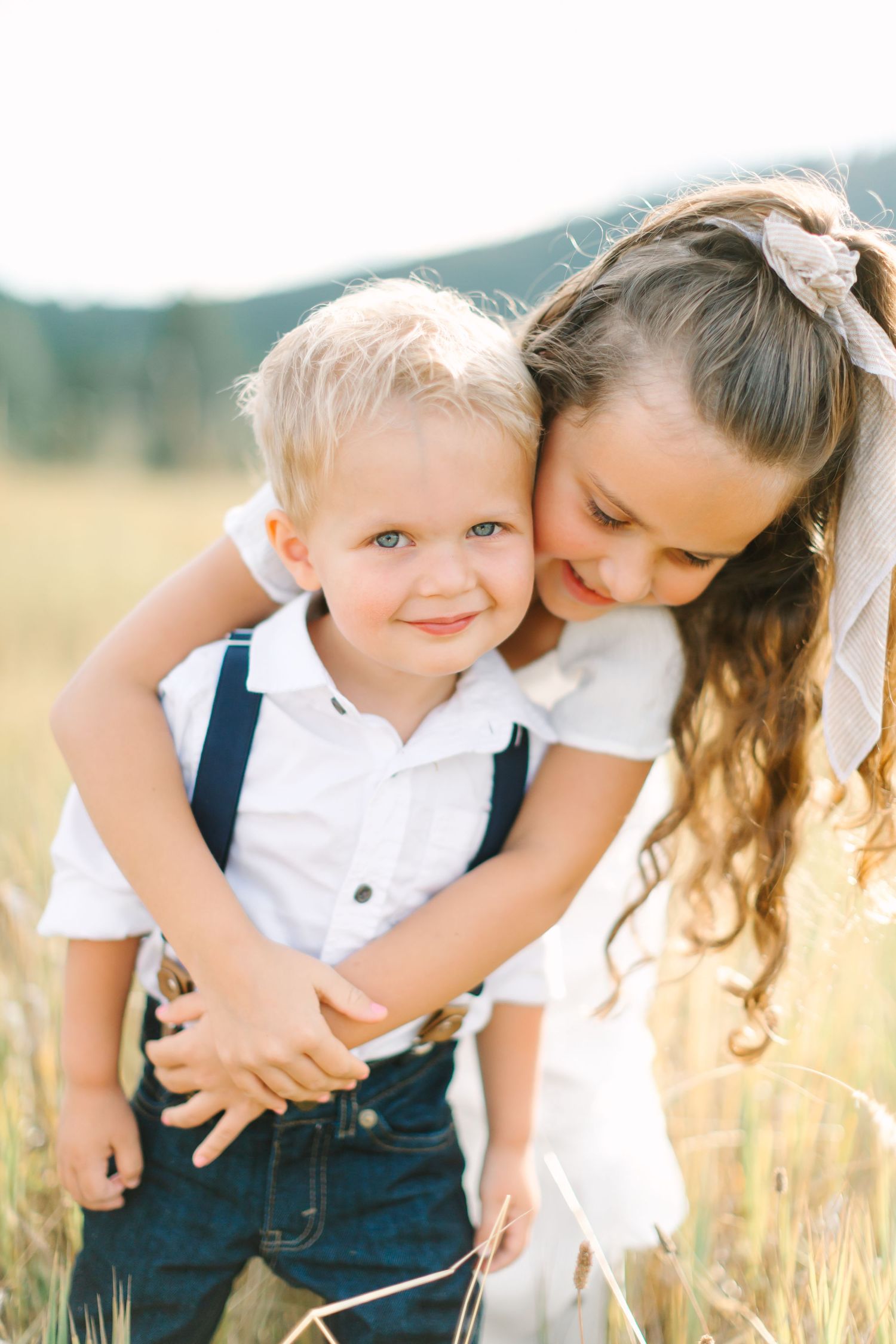 A tender moment captured in a golden wheat field shows two people embracing in matching white and navy outfits.