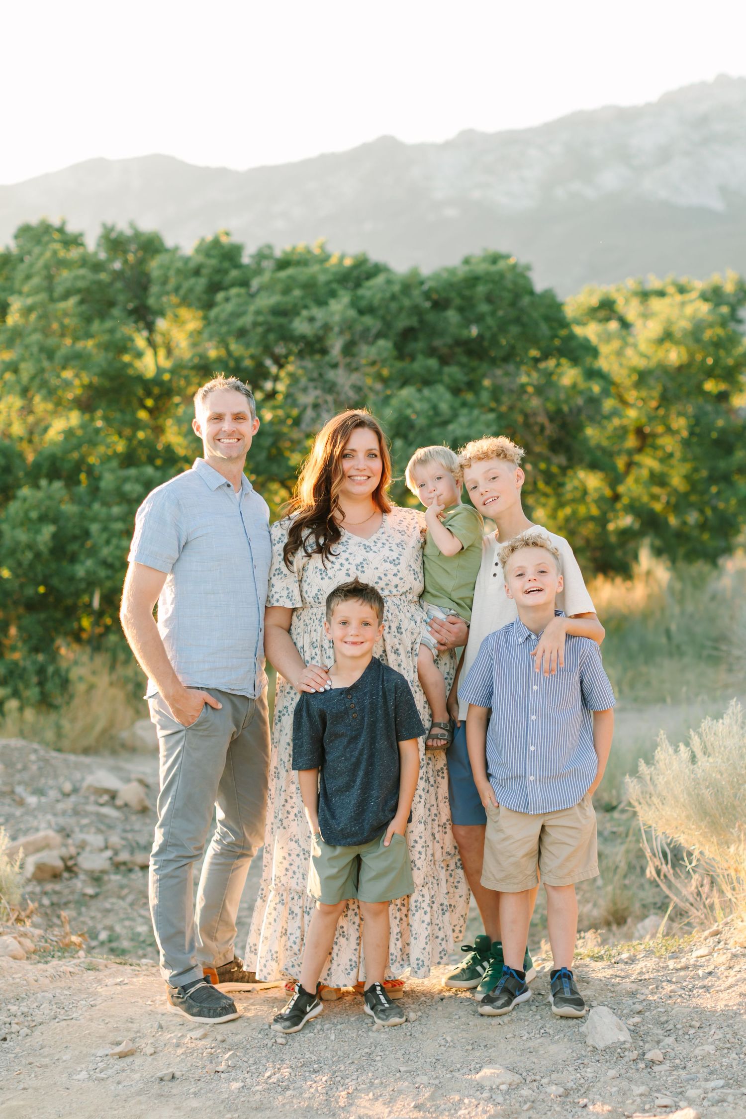 Family poses together outdoors during golden hour with mountains and trees in background.