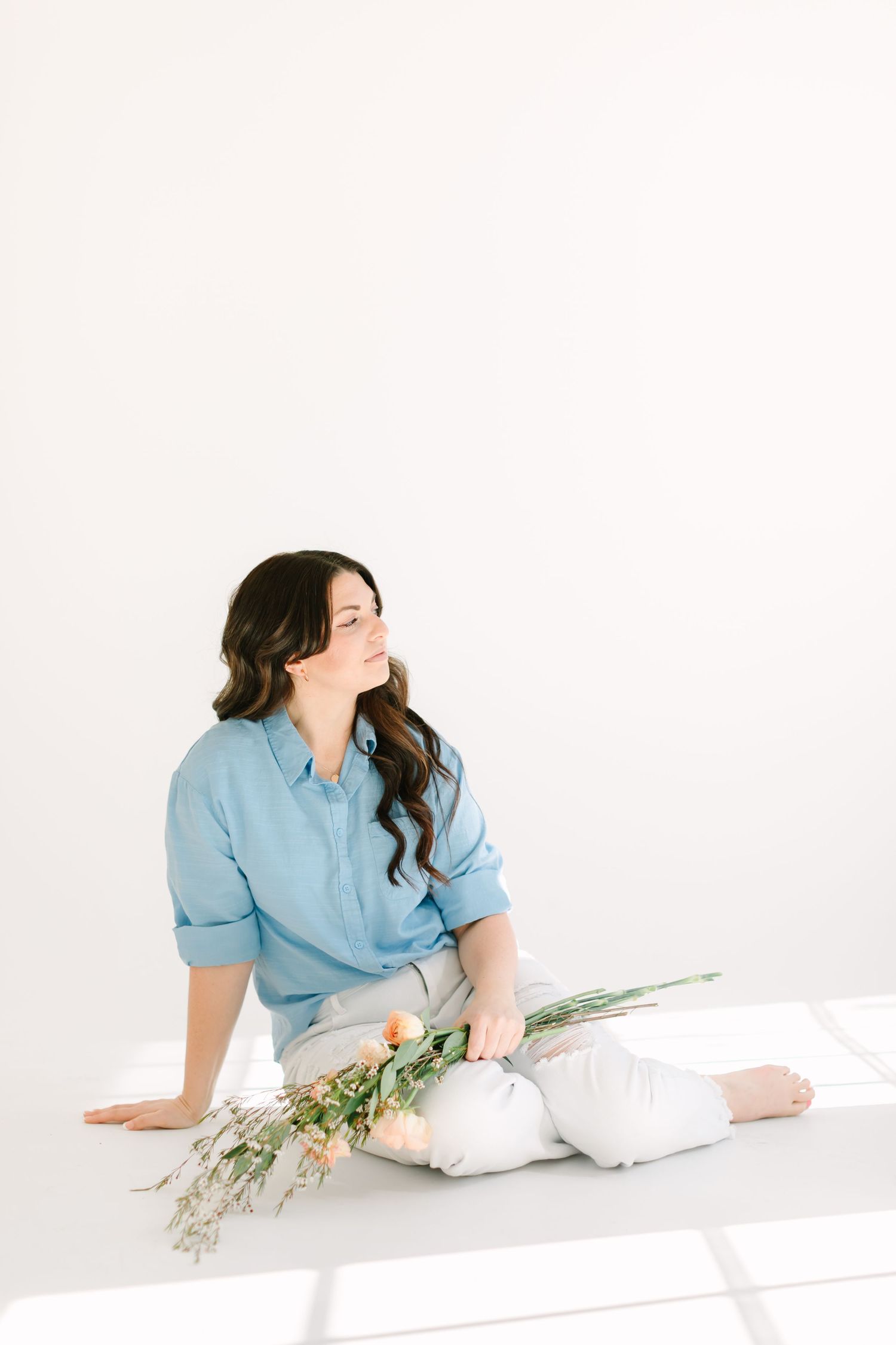 Person in light blue shirt reclining on white surface with yellow flowers in minimalist setting.