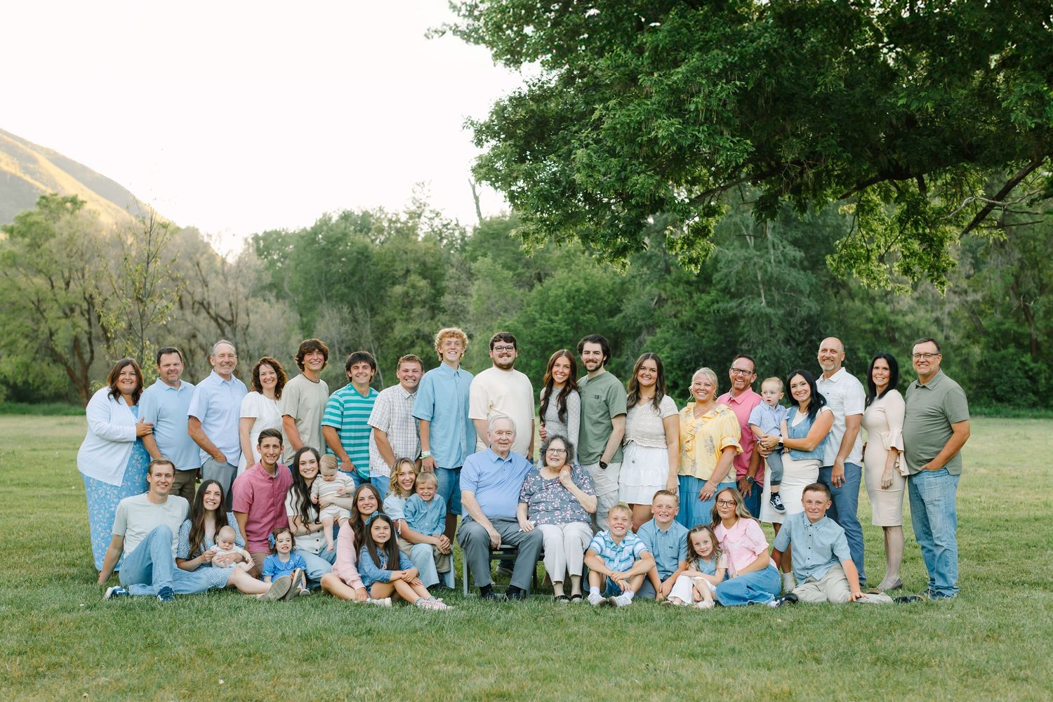 Large family group wearing coordinated pastel blue and white outfits poses together on grass for outdoor photo session.