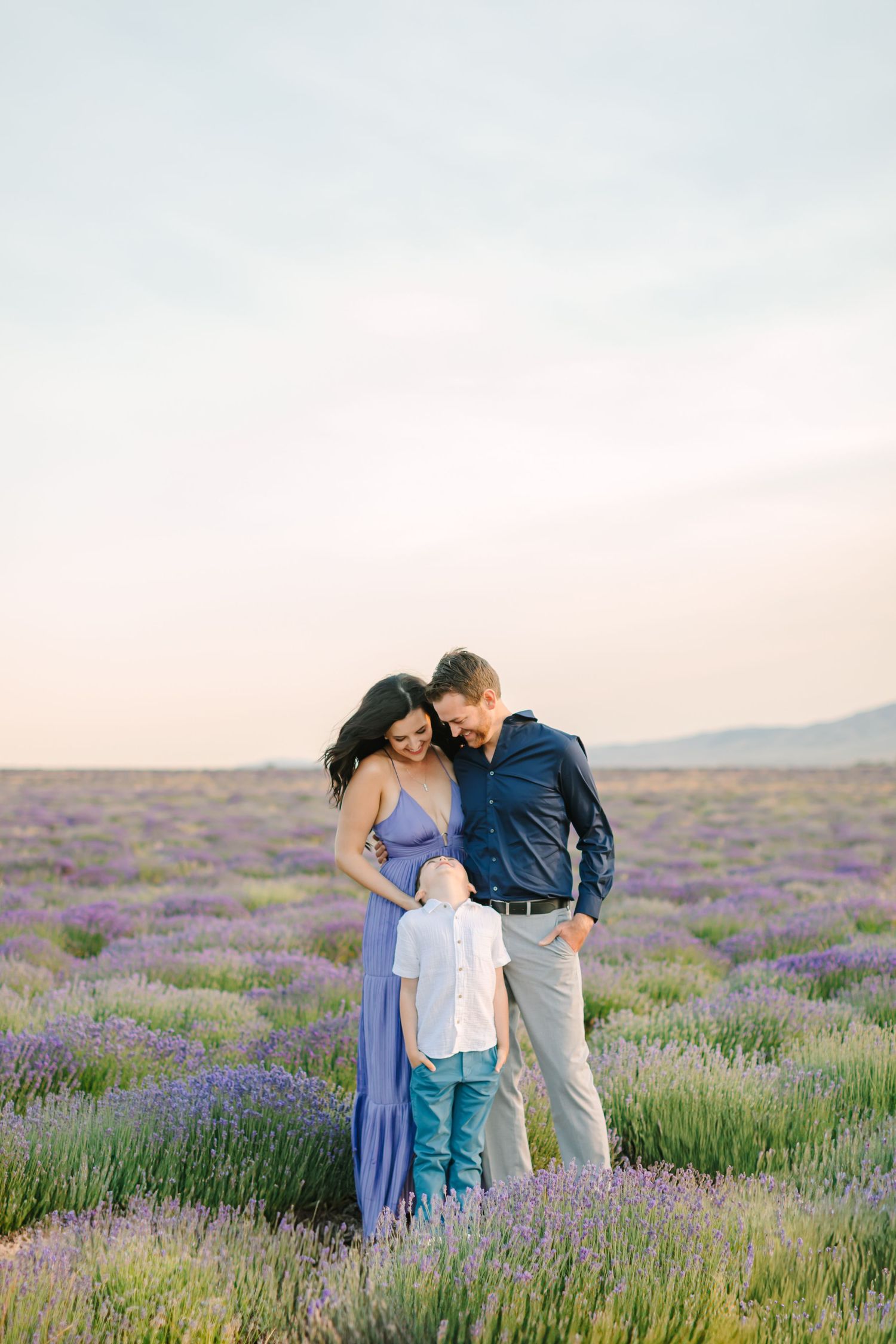A couple shares tender moments with their child in a blooming lavender field at sunset.