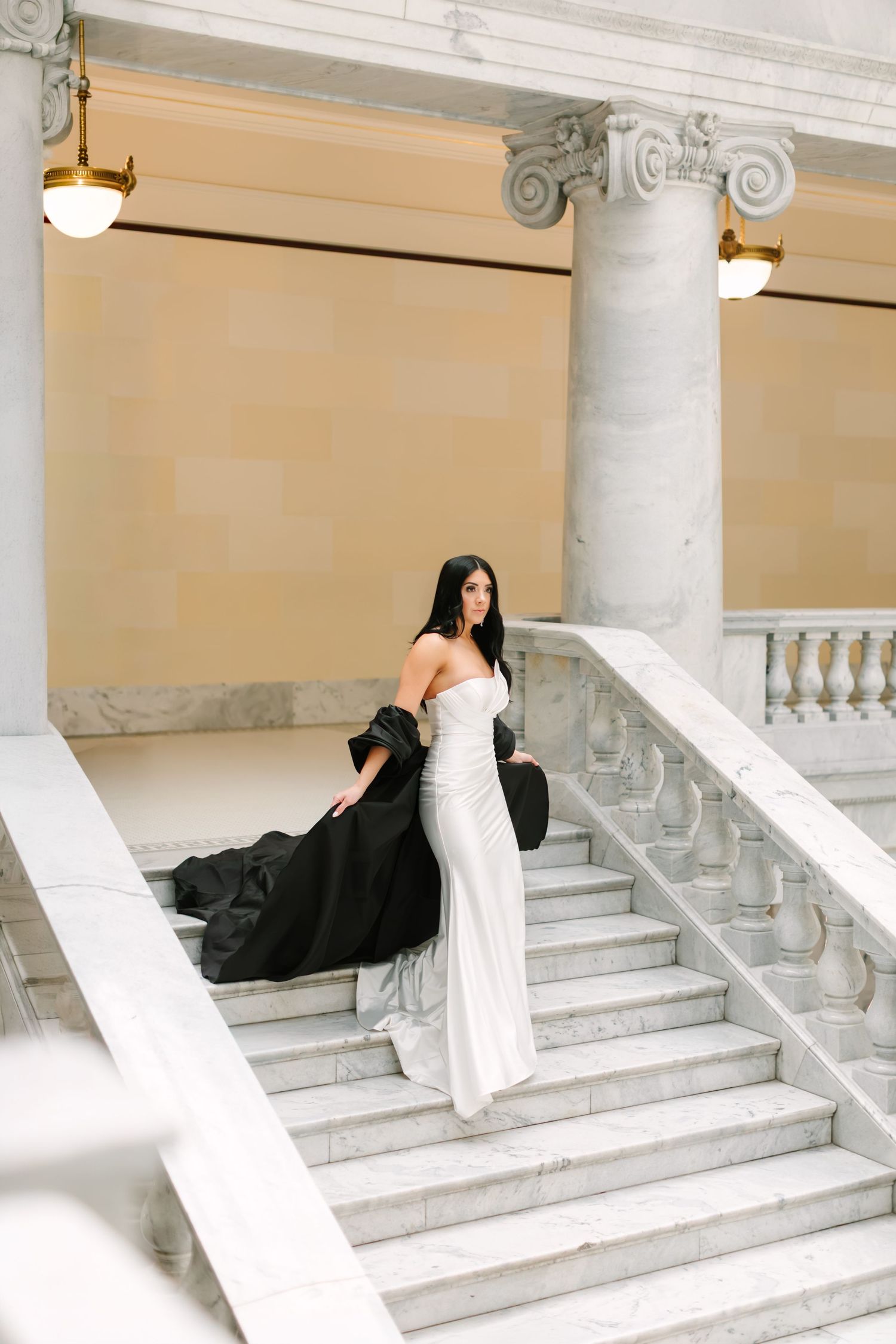 Woman in contrasting black and white dress poses gracefully on grand marble staircase in artistic photo series.