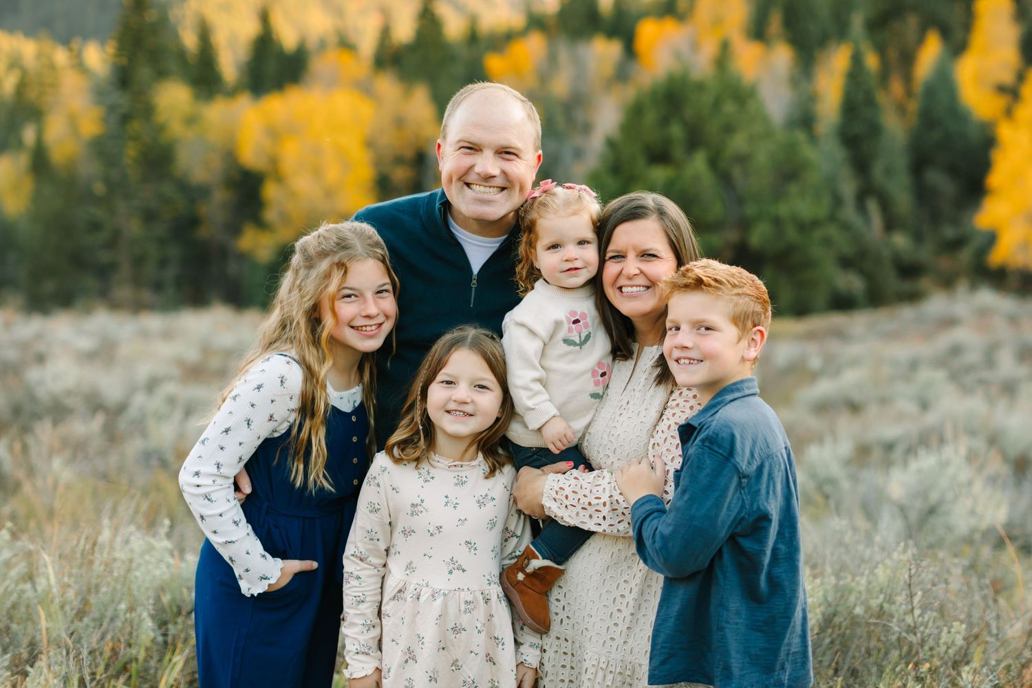 A family wearing coordinated blue and white outfits poses together in a golden autumn field at sunset.