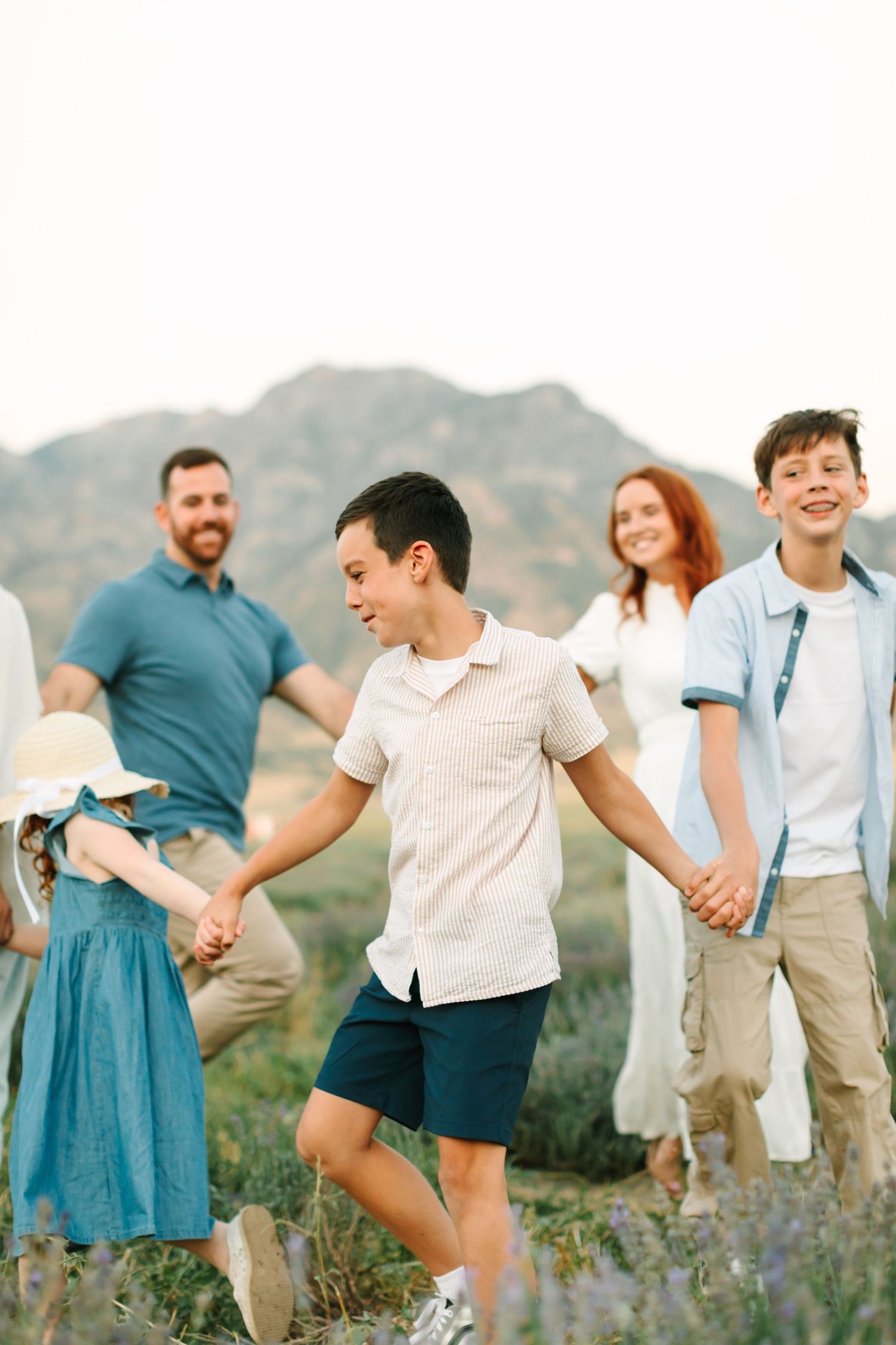 A group of people holding hands and dancing in a line against a mountain backdrop with wildflowers in bloom.