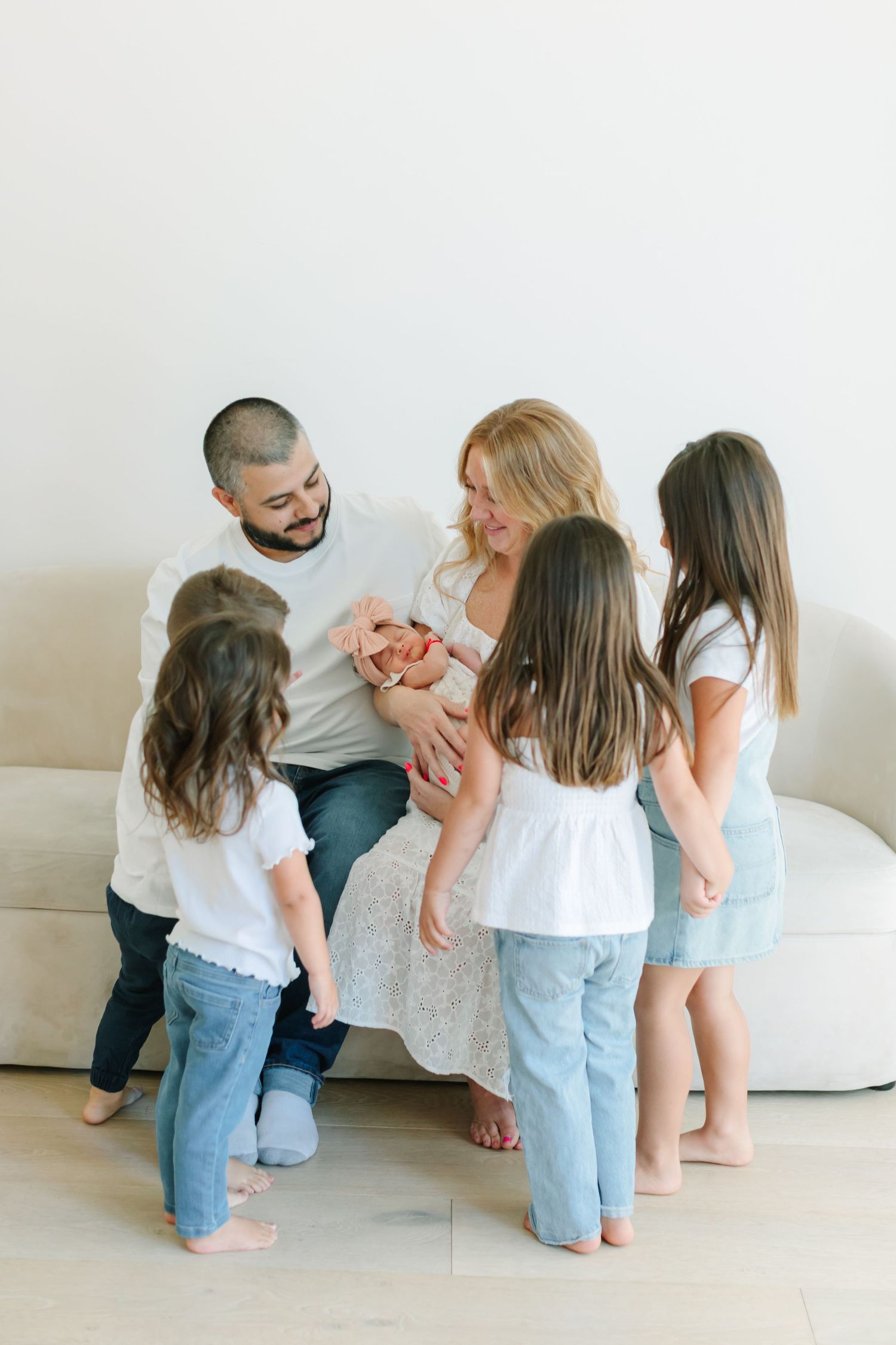 A family in matching white t-shirts and jeans shares playful moments together on a white couch in a series of photos.