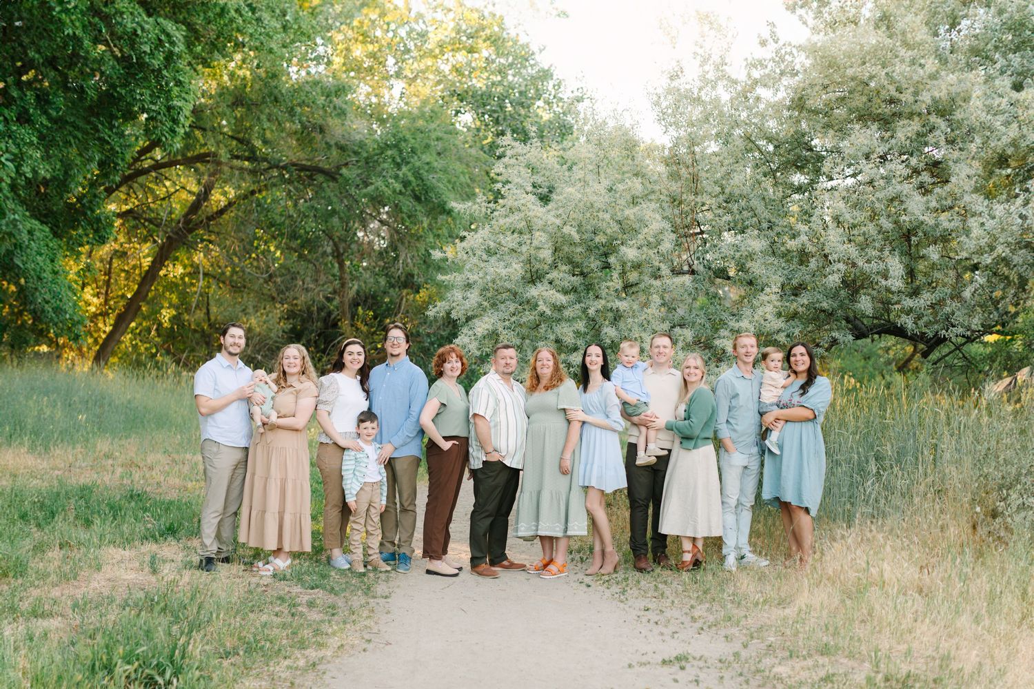 Wedding party in pastel attire poses together in a natural outdoor setting with green trees and foliage.