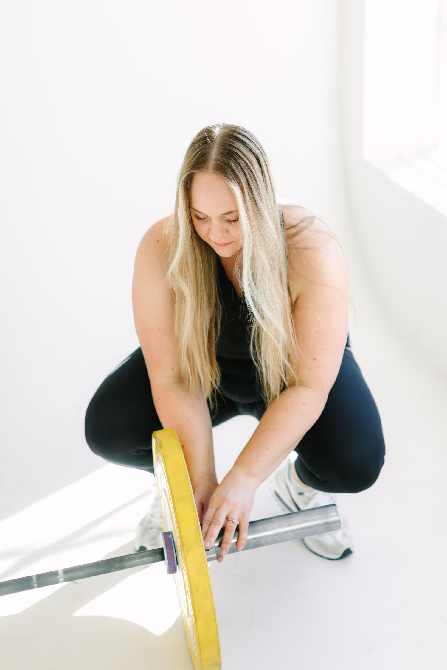 Woman in black workout attire using a resistance band while exercising on a bench in a bright white room.