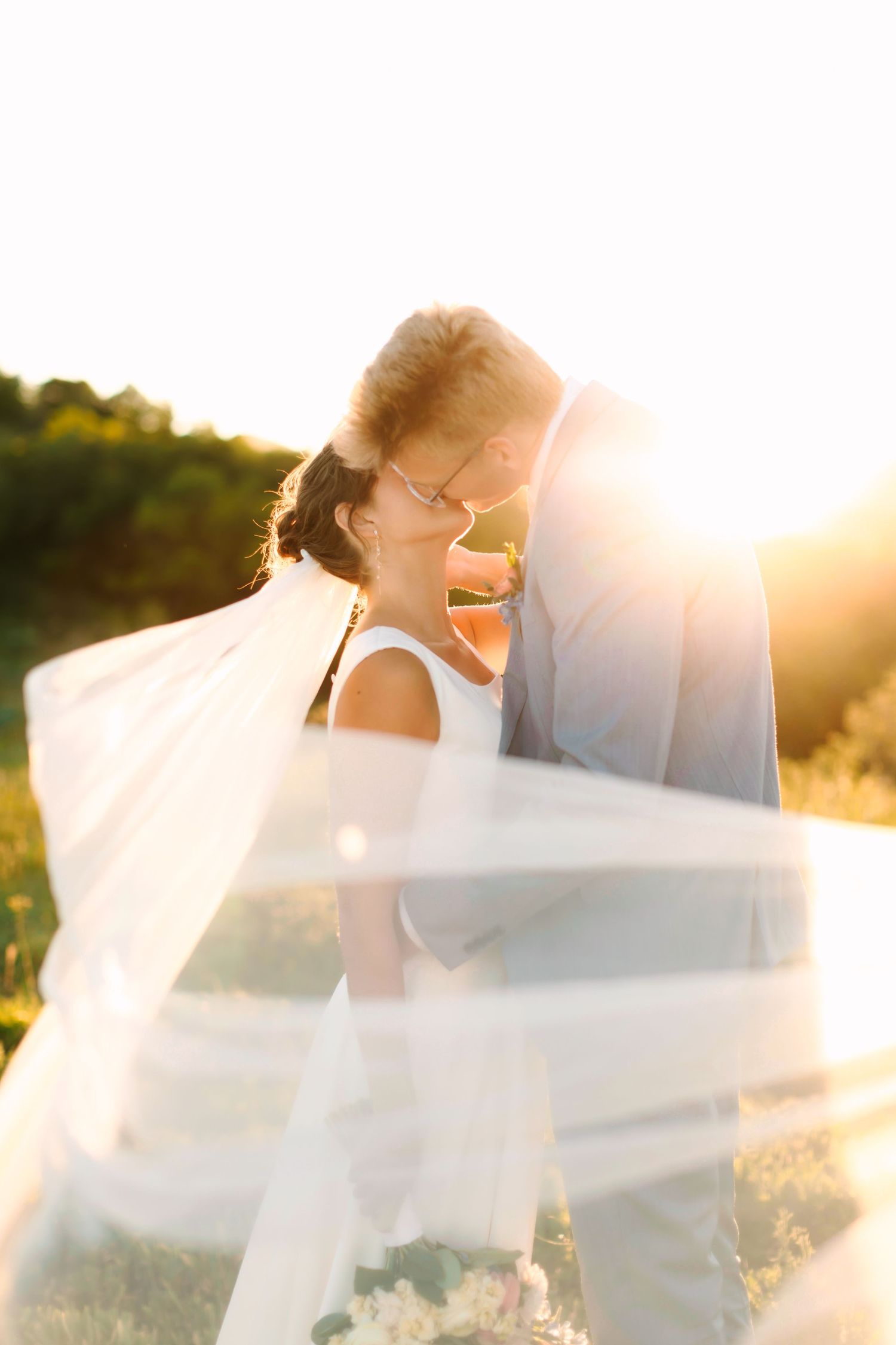 Bride and groom share a romantic moment bathed in golden sunset light with veil flowing around them.