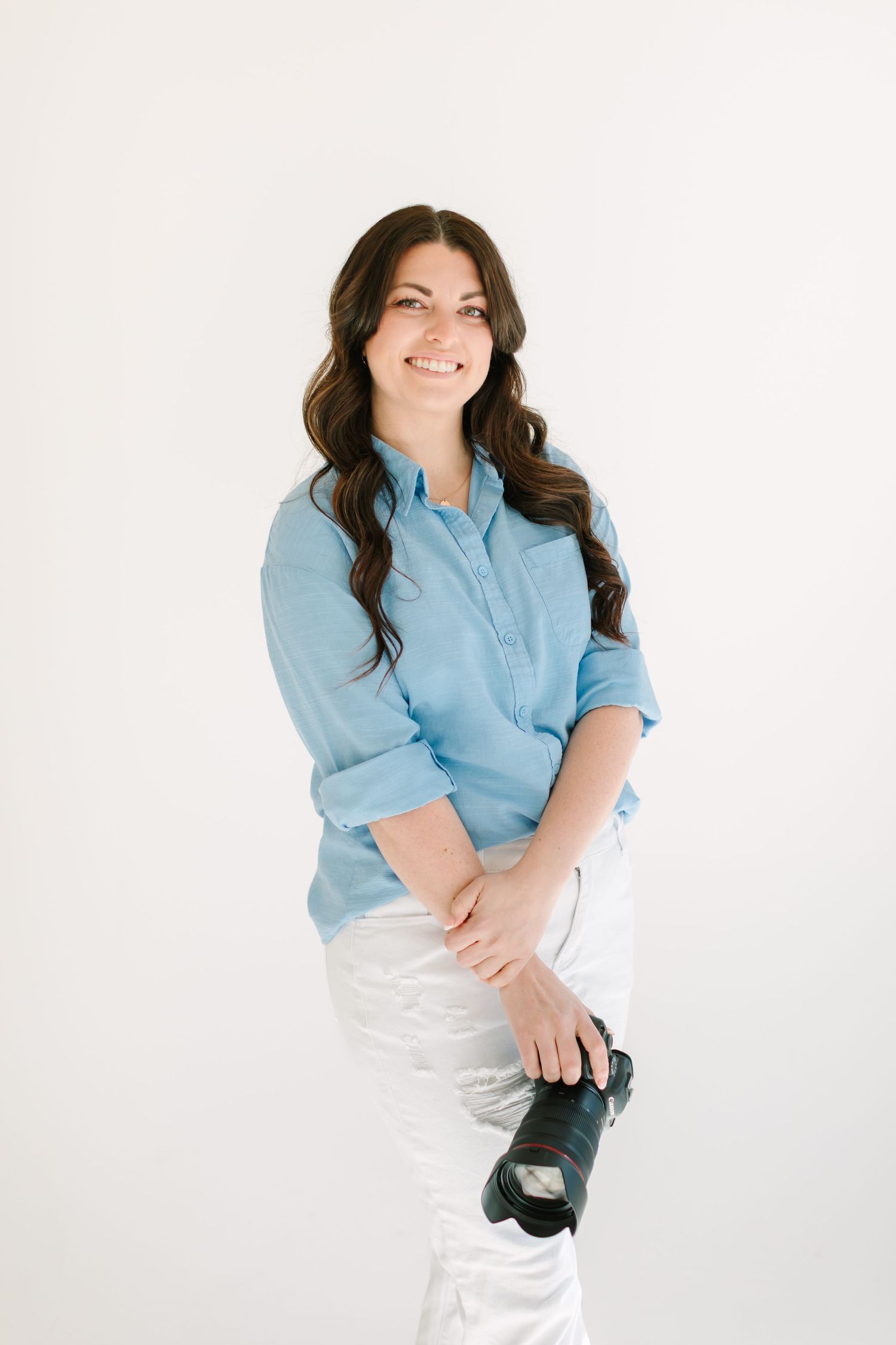 Professional studio portrait of person in light blue button down shirt and white pants against white backdrop.