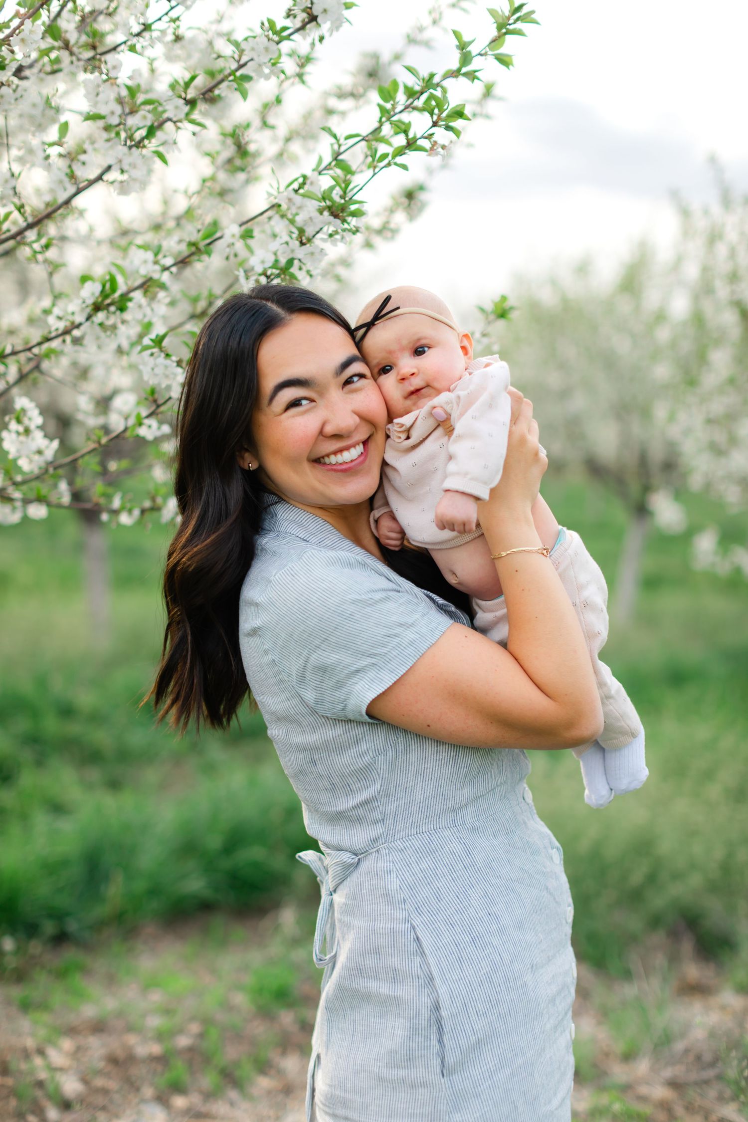 Parent and baby share joyful moments together in a blooming spring orchard with white flowers.